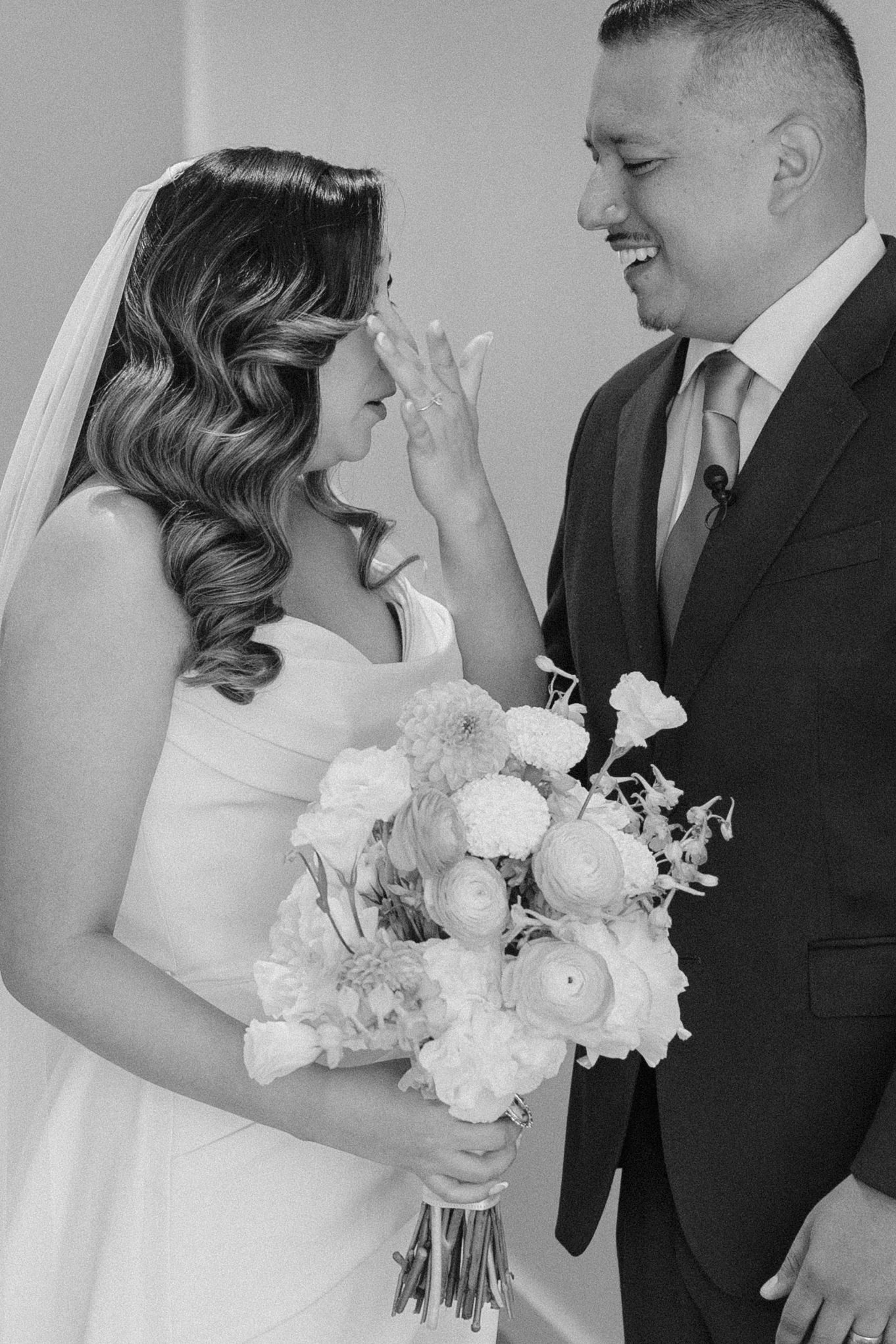 Black and white photo of a bride and groom sharing an emotional first look moment, bride holding a floral bouquet.