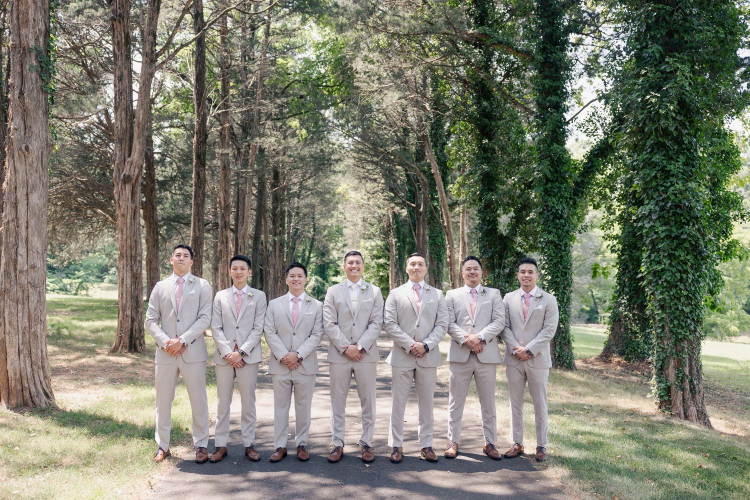 Wedding party in light gray suits standing in a row among tall pine trees.