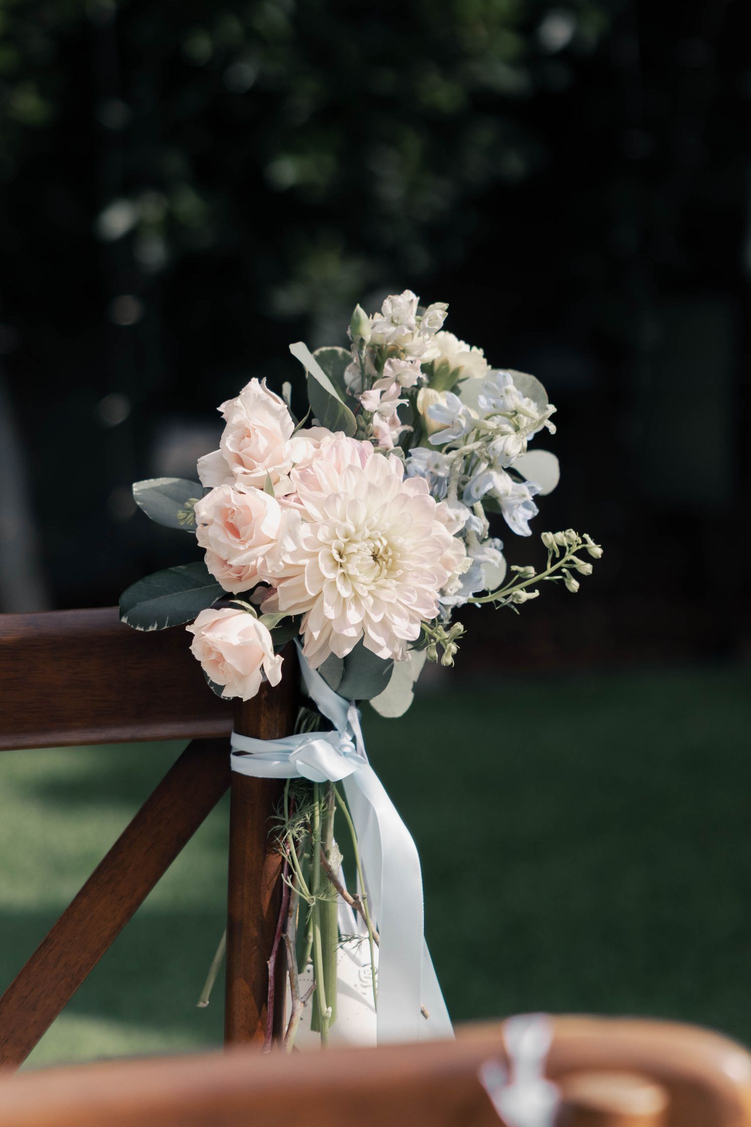 A delicate arrangement of pink roses and white peonies in a glass vase adorns a wooden chair outdoors.