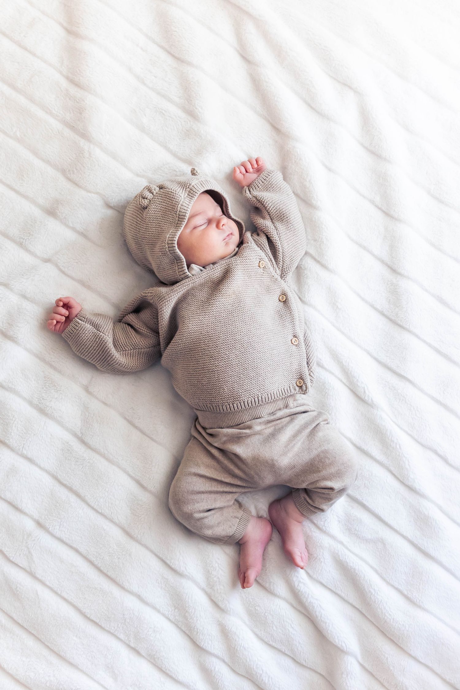Baby lying on white textured bedding wearing a cozy gray outfit.