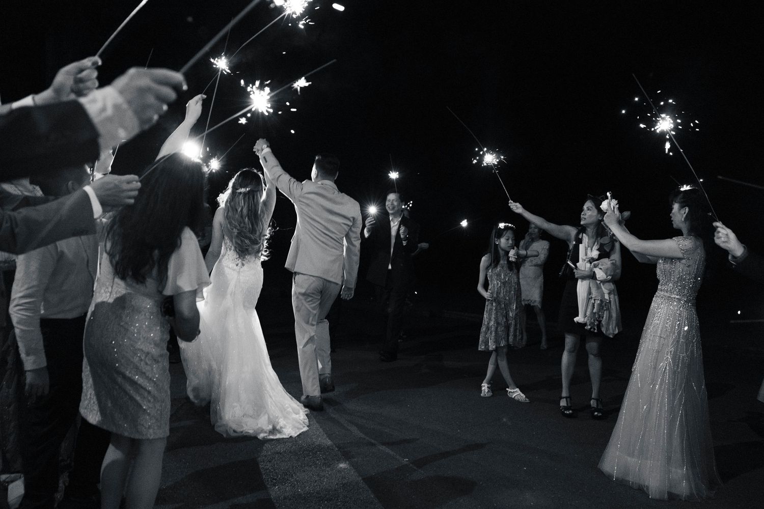 Wide shot of wedding guests holding sparklers during nighttime celebration as the couple does a sparkler exit.