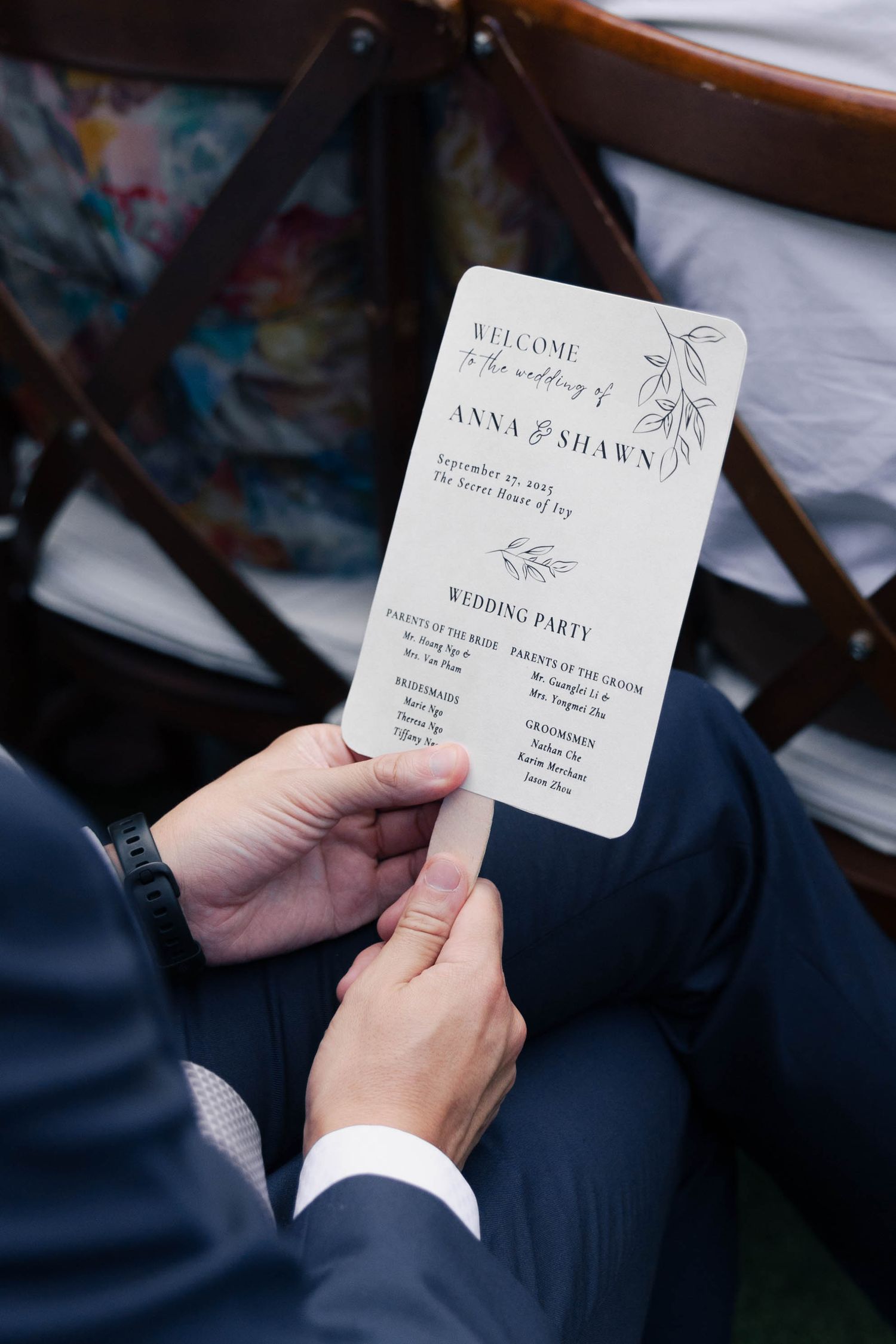 A hand holds an elegant wedding party program card with delicate floral details against a blurred background.