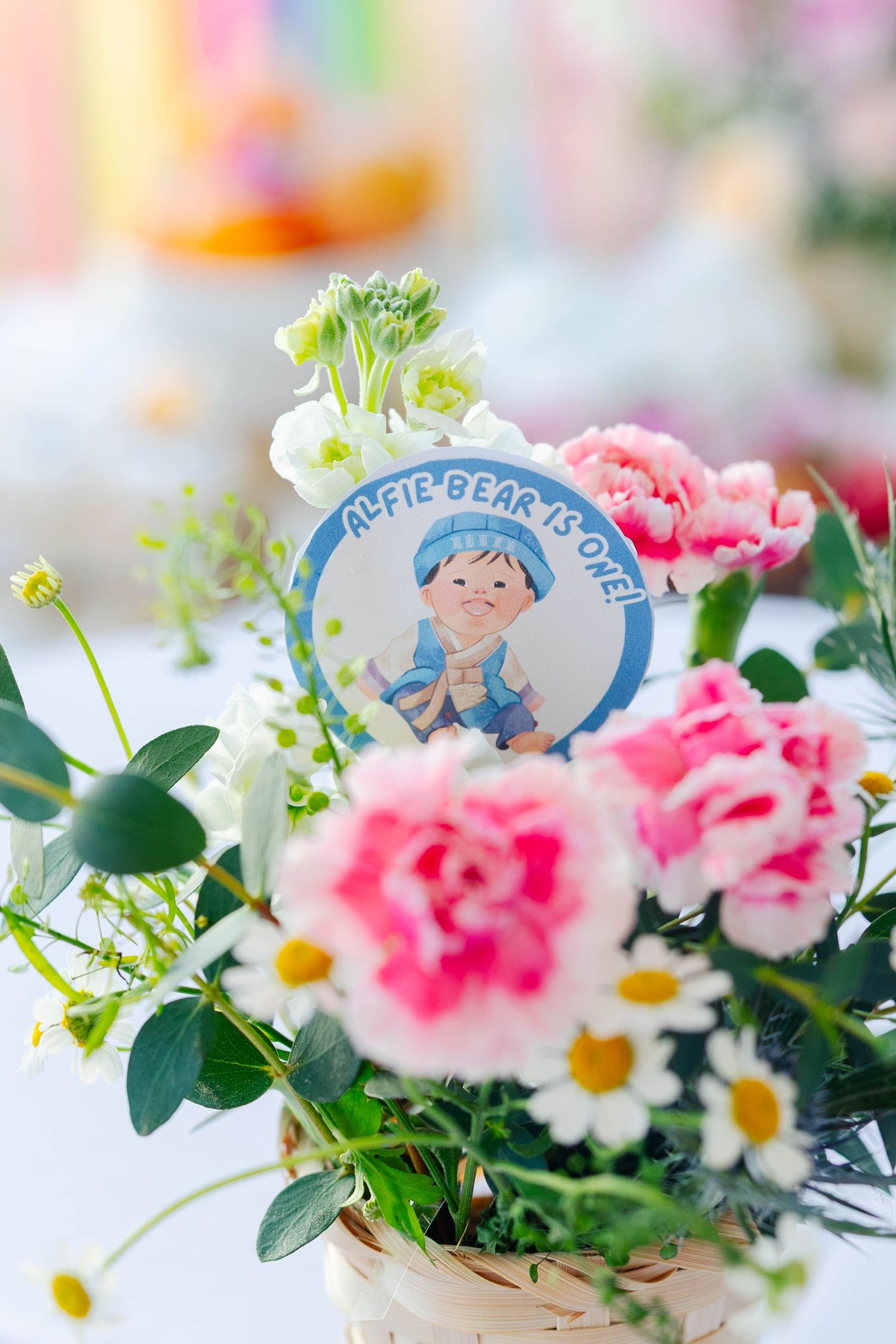 Delicate pink and white flowers arranged with greenery and decorated with blue wedding favor tags on a light background.