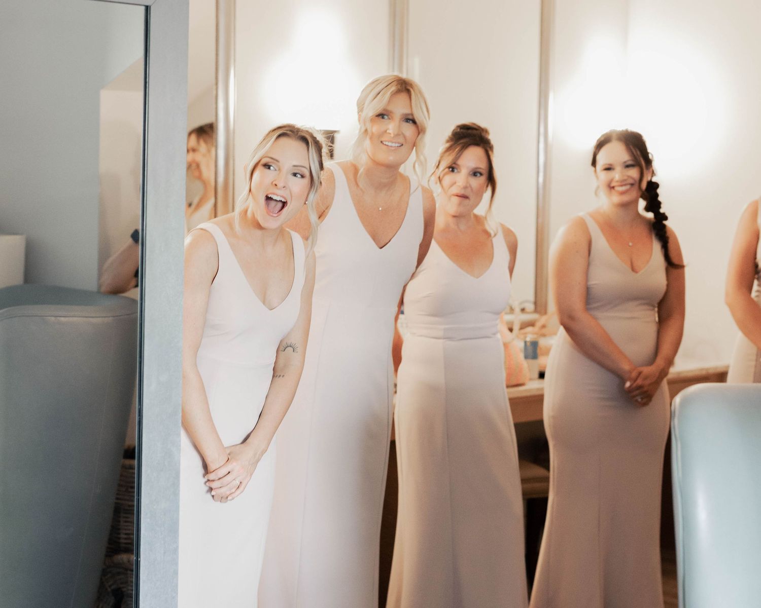 Bridesmaids in neutral colored dresses stand together during wedding preparations.