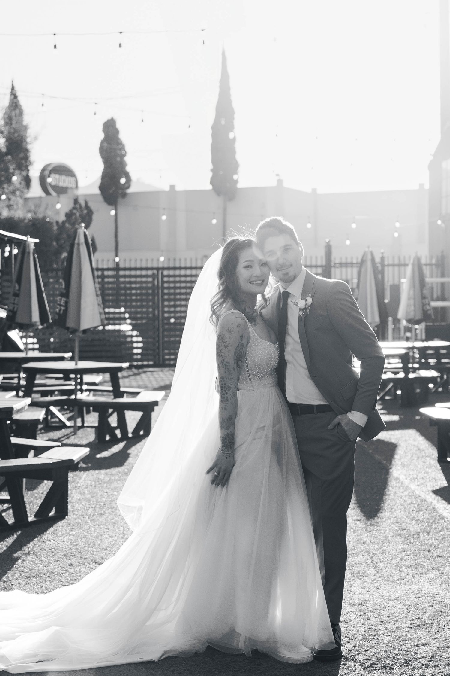 Wedding couple sharing tender moments in sunlit outdoor venue with picnic tables.