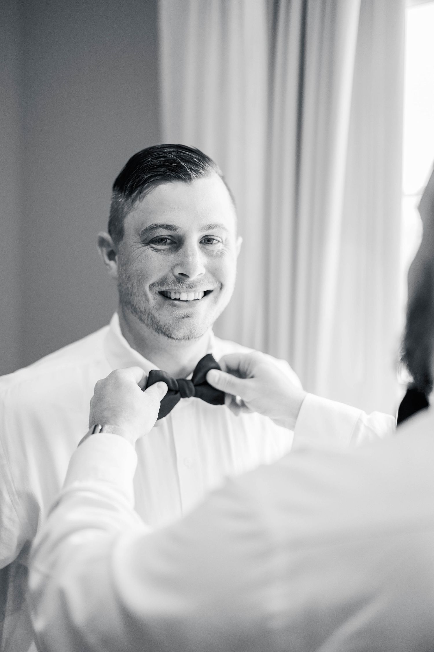 Candid moment during wedding preparations showing genuine smile and formal wear.