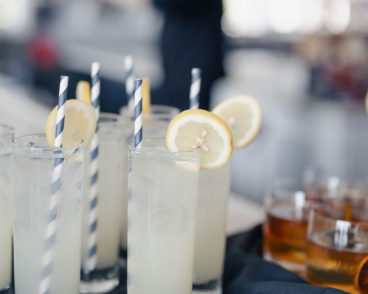 Row of refreshing cocktails with blue striped straws served on a dark surface.