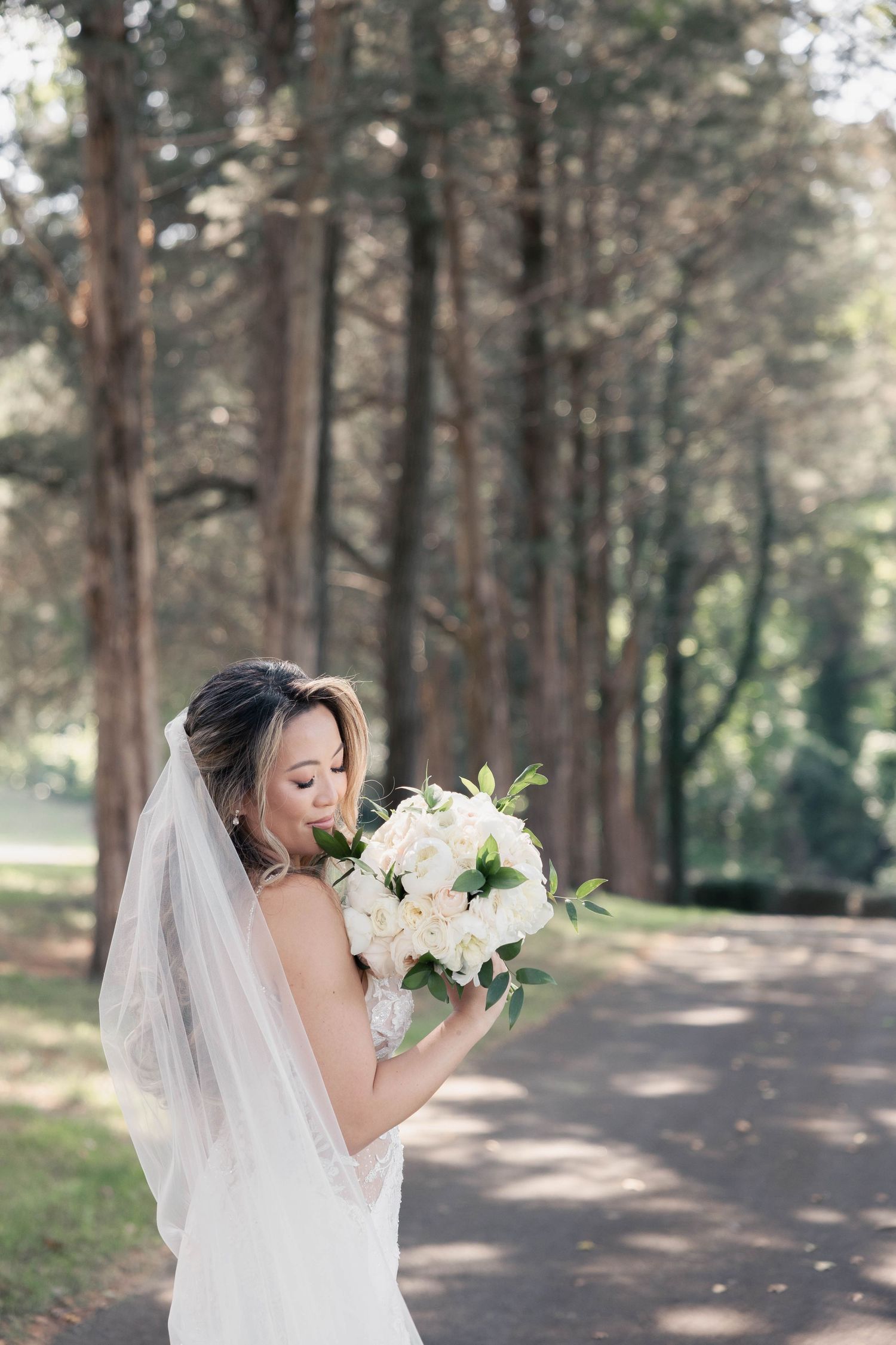 Romantic bridal portrait in wooded setting with delicate veil and white floral bouquet.