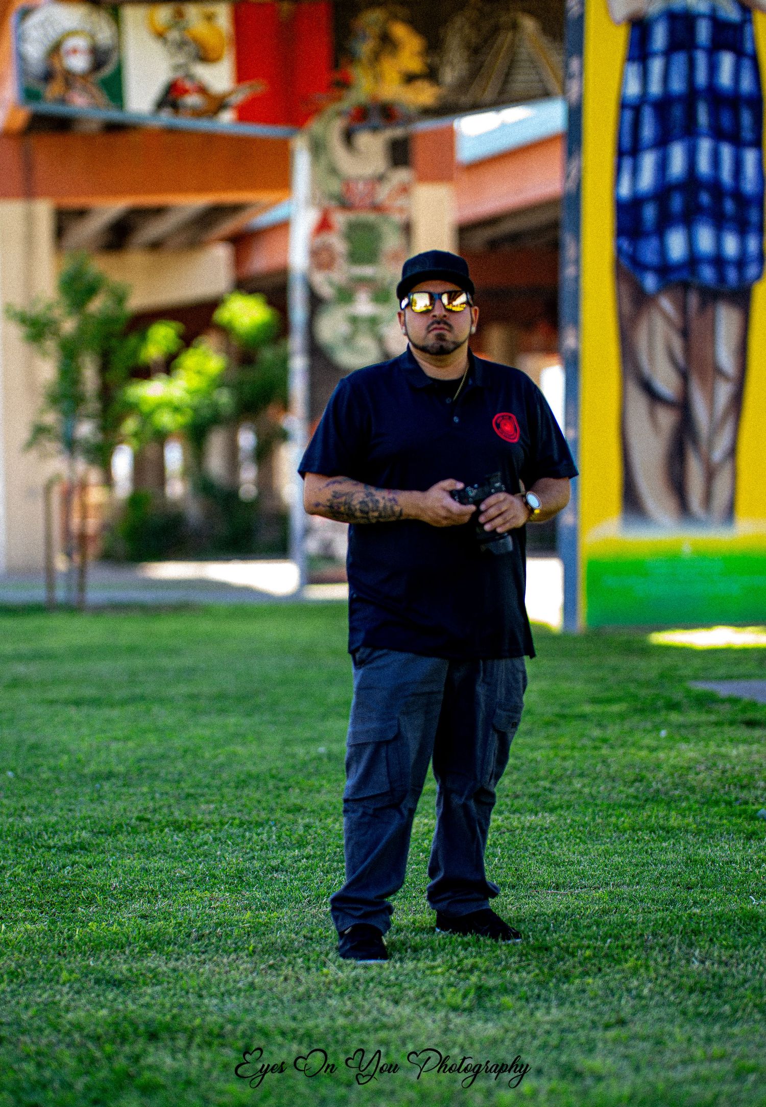Figure in dark clothing seated outdoors against colorful building backdrop.