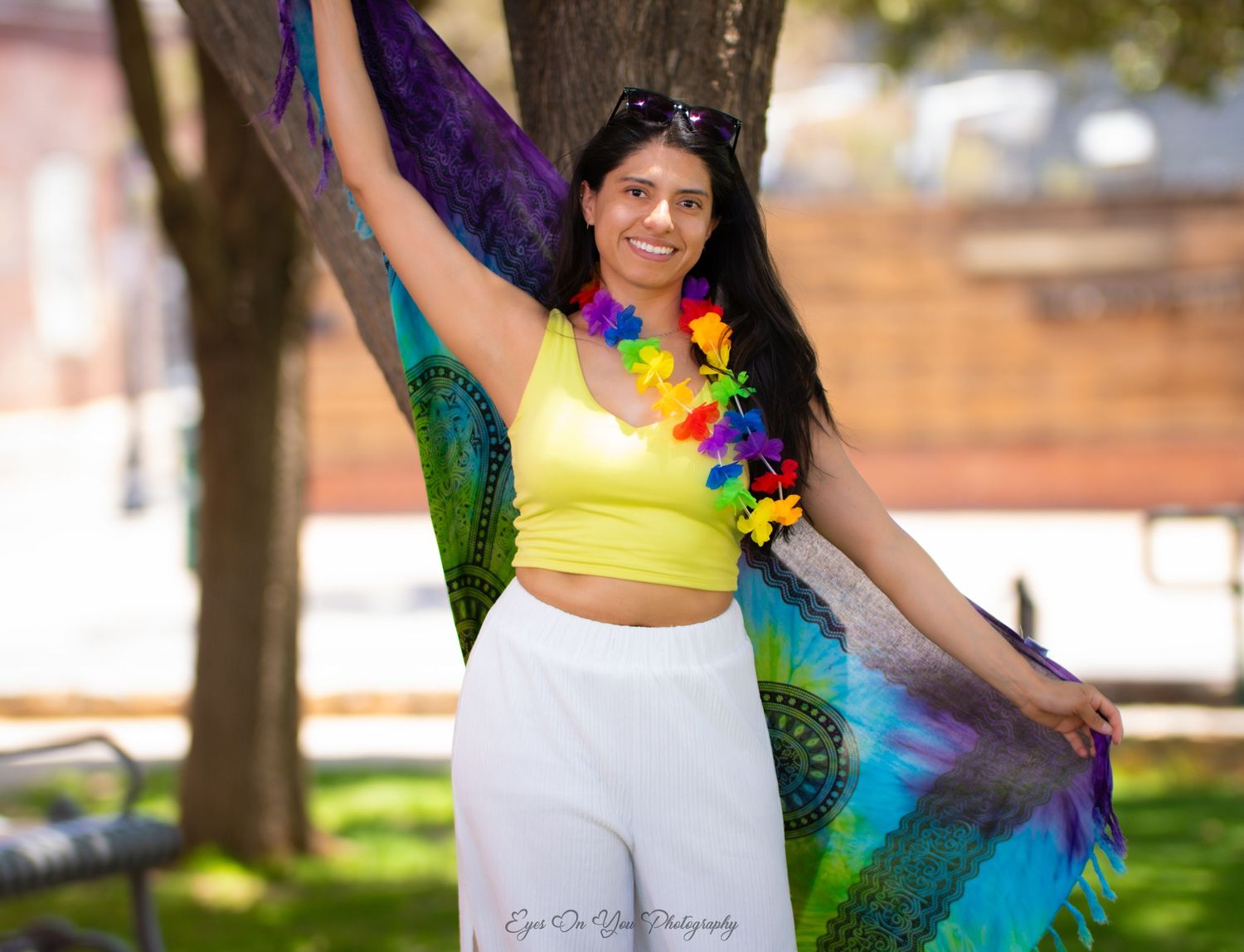 A festive street photo featuring colorful rainbow fabric and a yellow crop top against a sunny outdoor backdrop.
