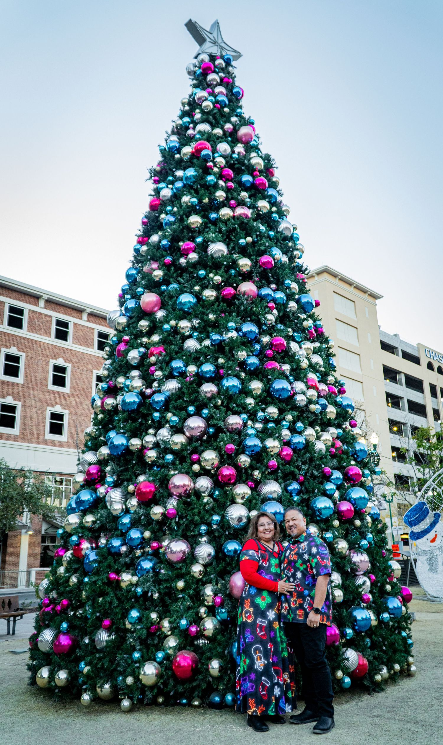 Festively decorated Christmas tree with pink and blue baubles displays against urban backdrop.