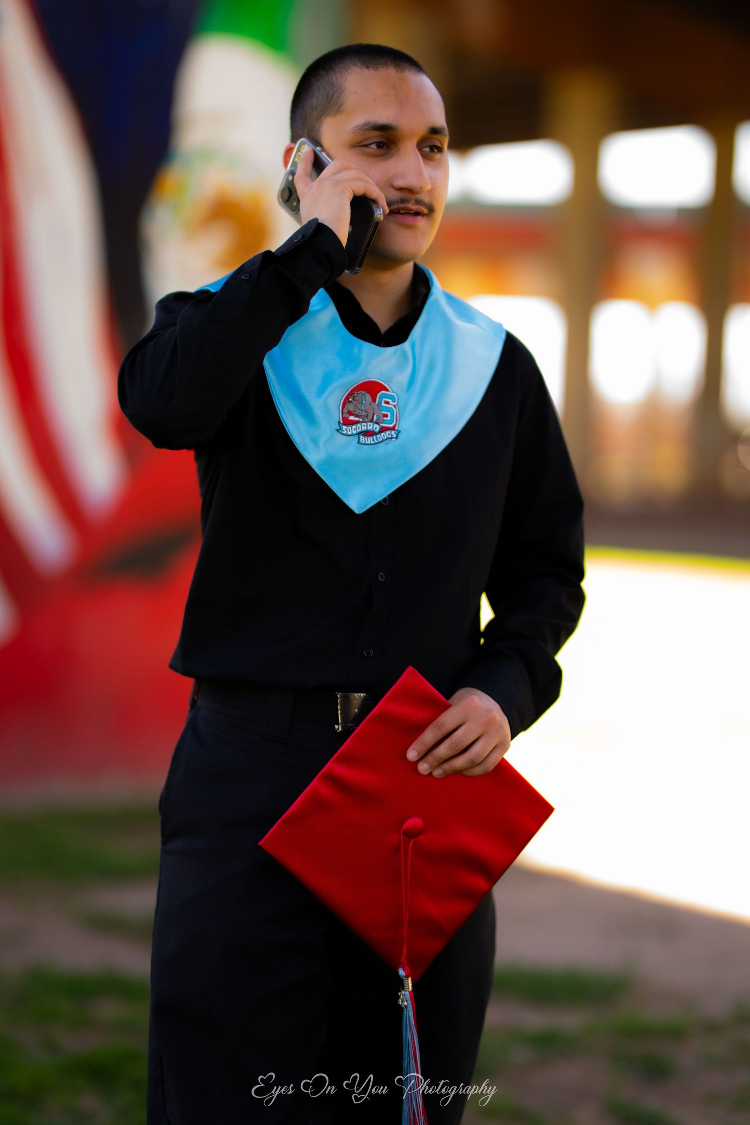 Graduate in red and blue regalia posing against colorful background.