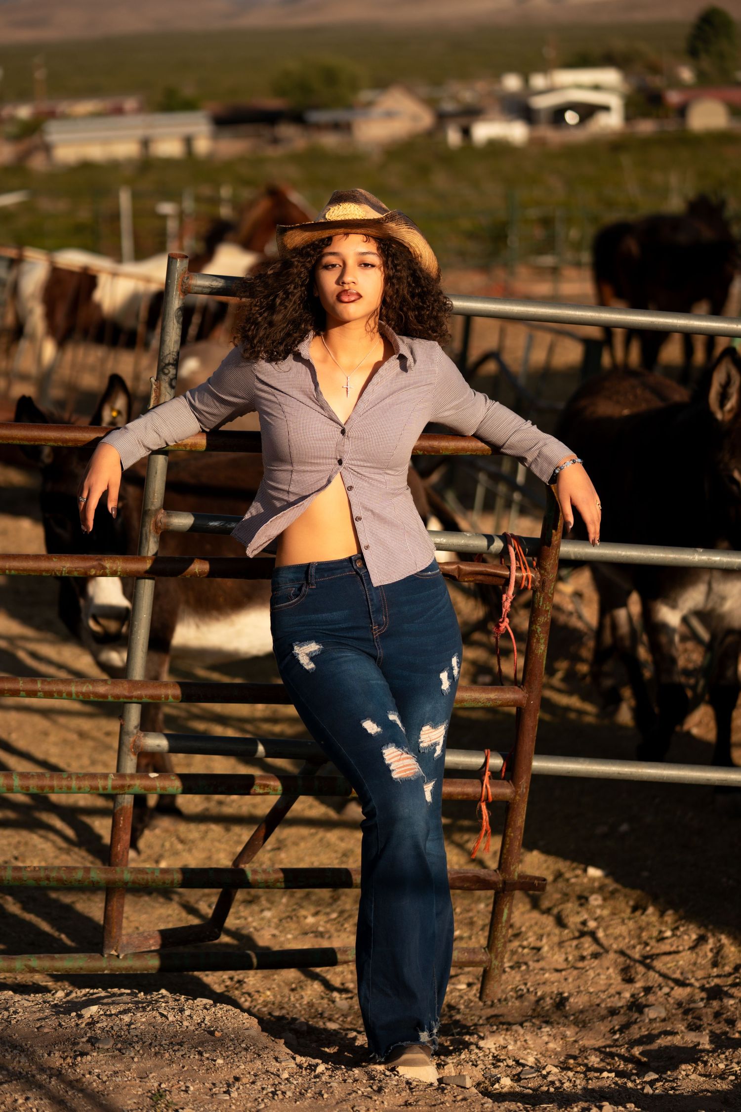 Stylish country fashion pose against ranch fencing with mountains and houses in background.