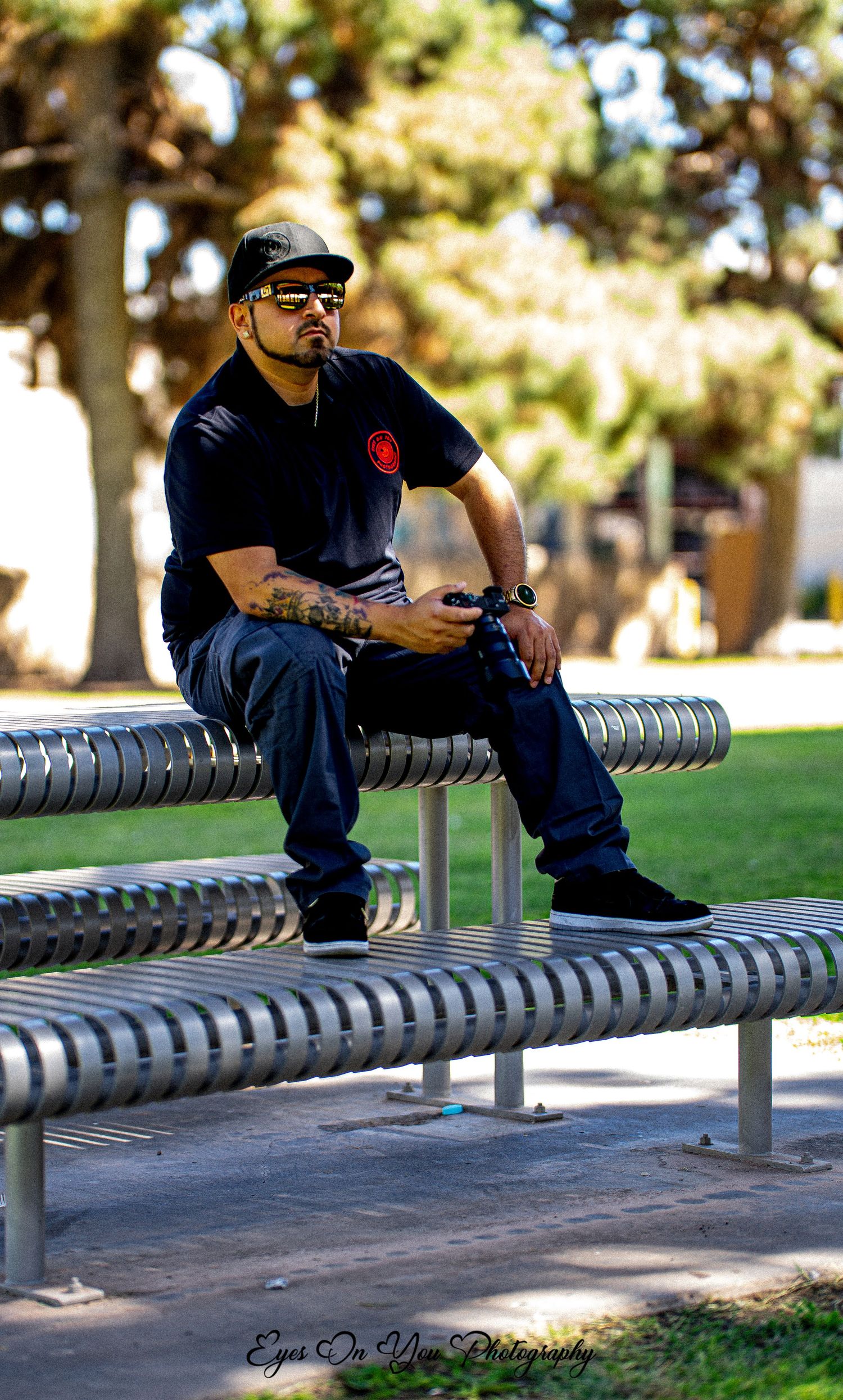 Person seated on metal bench against sunny outdoor background.
