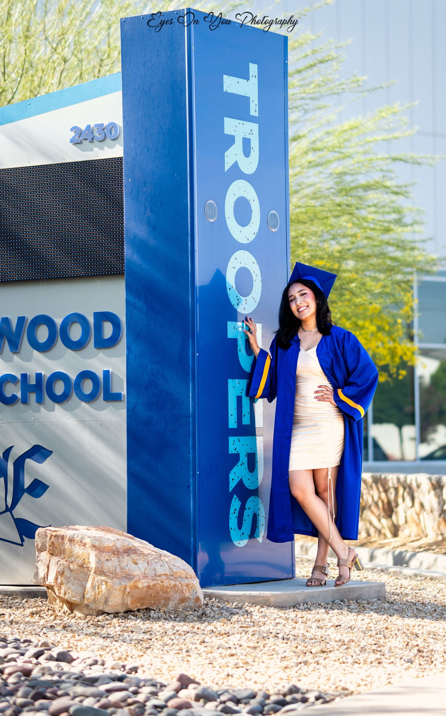 Blue graduation gown contrasts against Eastwood High School exterior signage during photo session.
