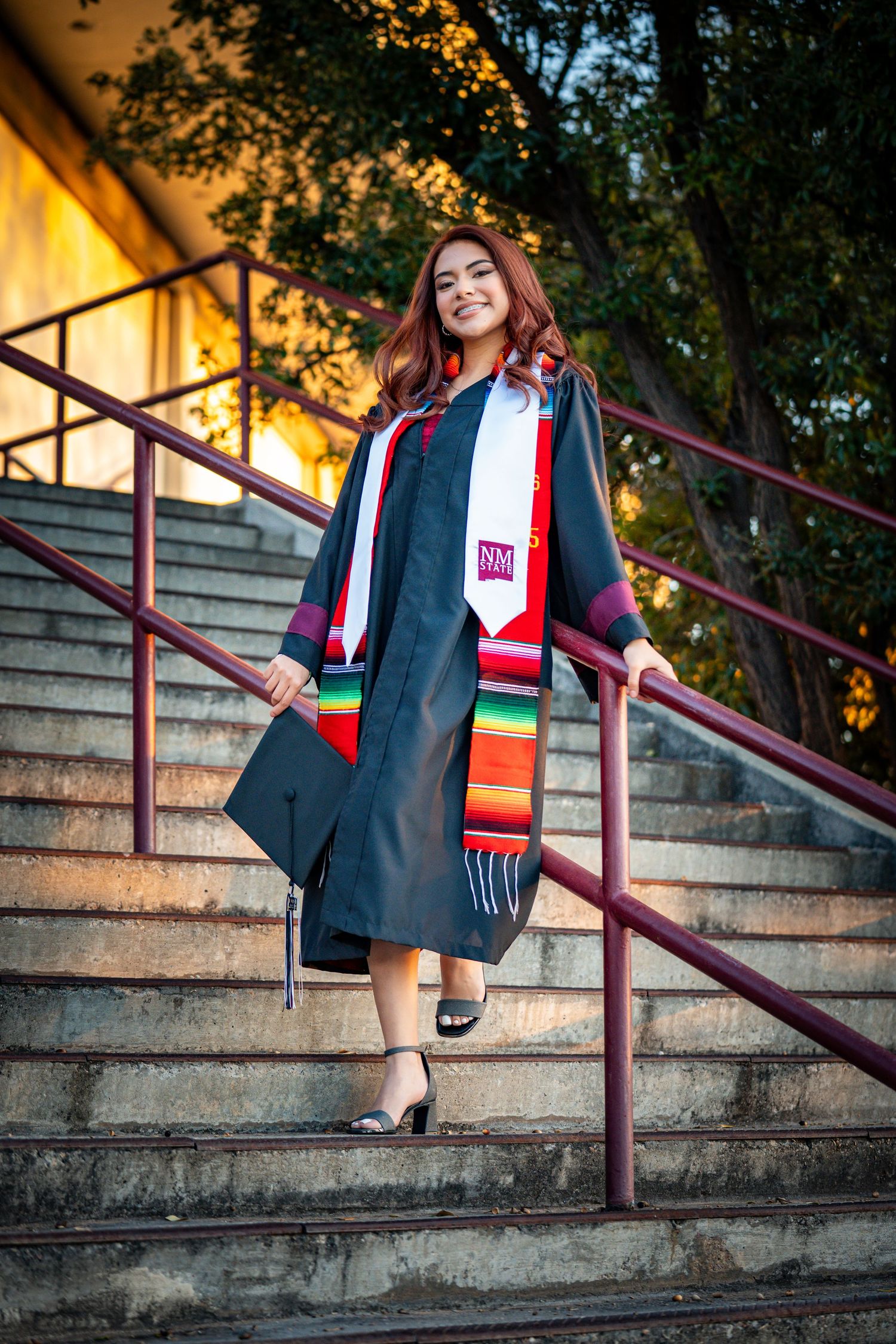Graduation photos on concrete steps showing graduate in cap and gown with colorful stole at golden hour.