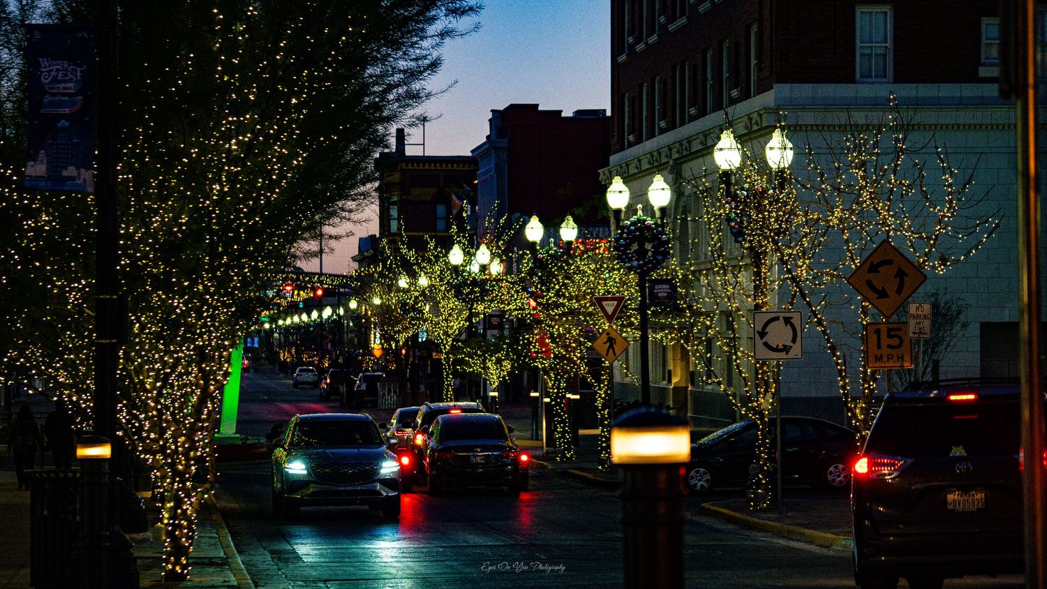 City street decorated with holiday lights and glowing lampposts reflecting off wet pavement.