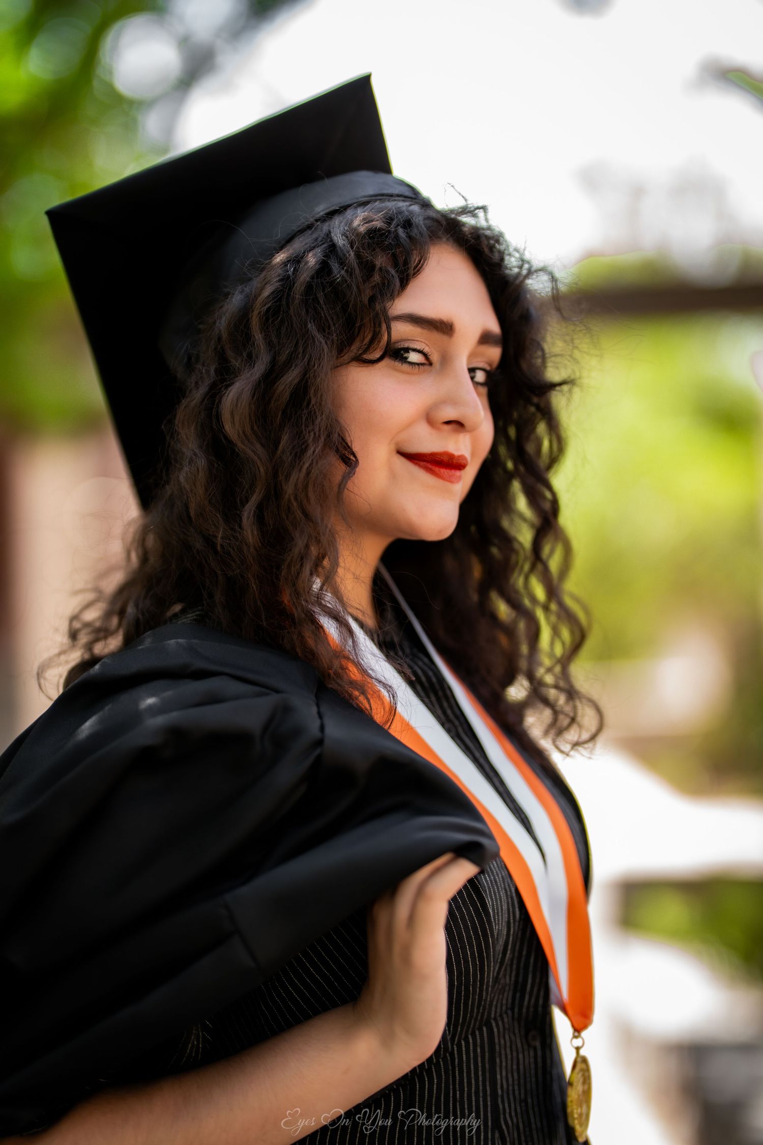 Graduate in academic regalia with curly hair and black cap showcasing decorative graduation stole.