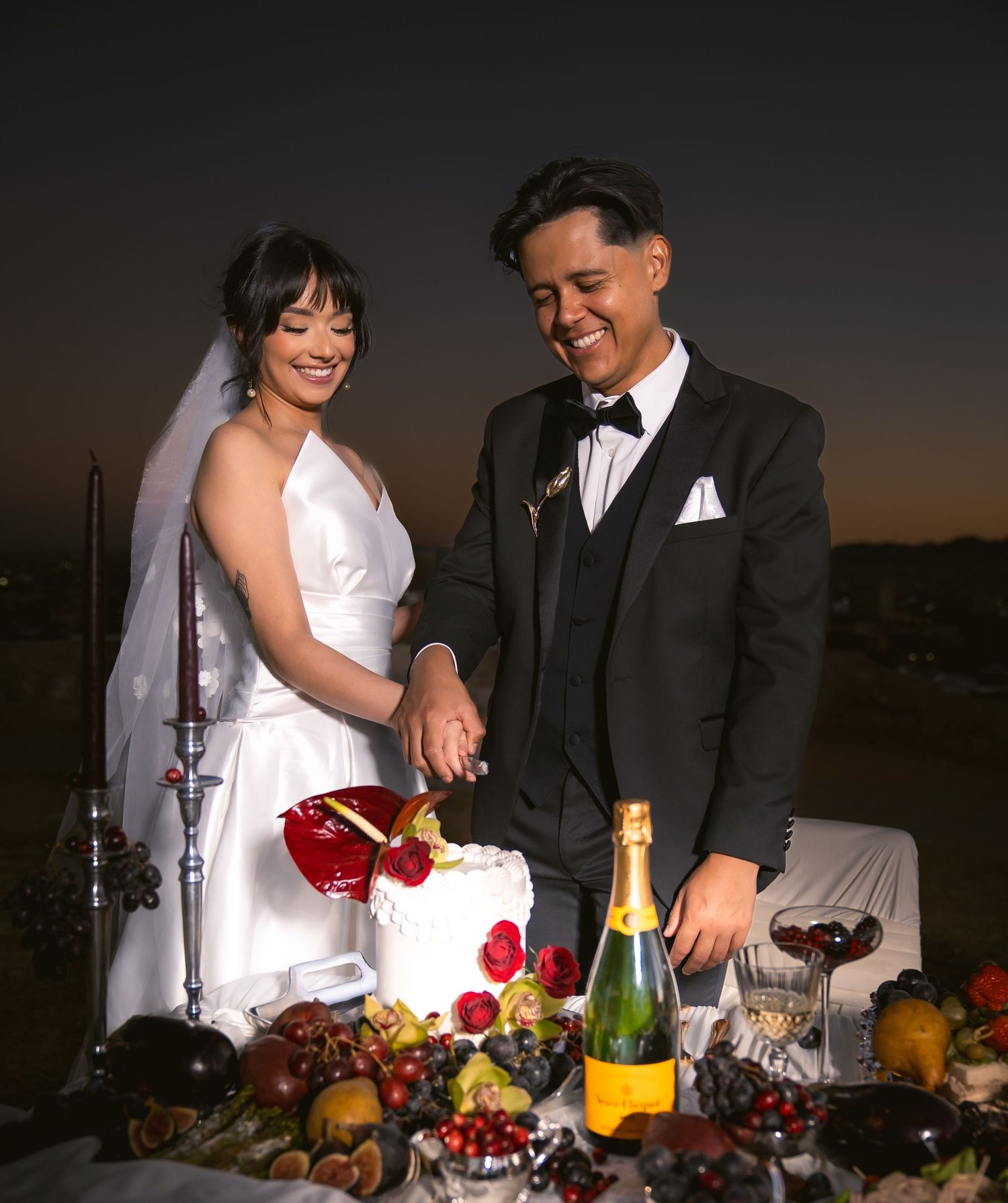 Newlyweds celebrate with champagne and fresh fruit at an elegant outdoor reception table at sunset.