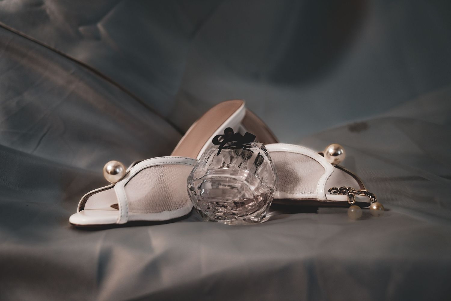 A silver spider ring with intricate details and gemstone accents rests on a reflective surface in moody lighting.