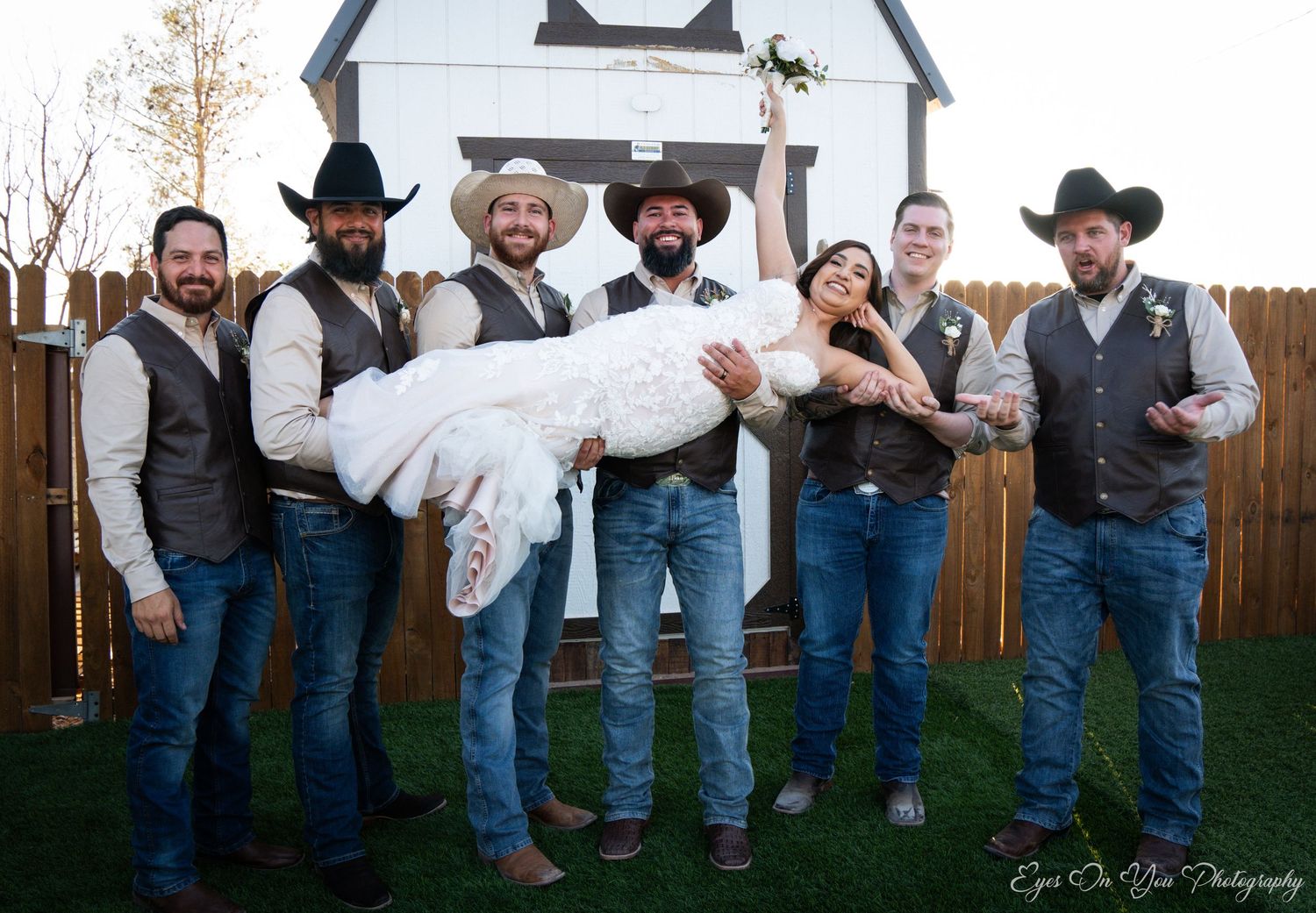 Wedding party line-up against a white barn wall outdoors.