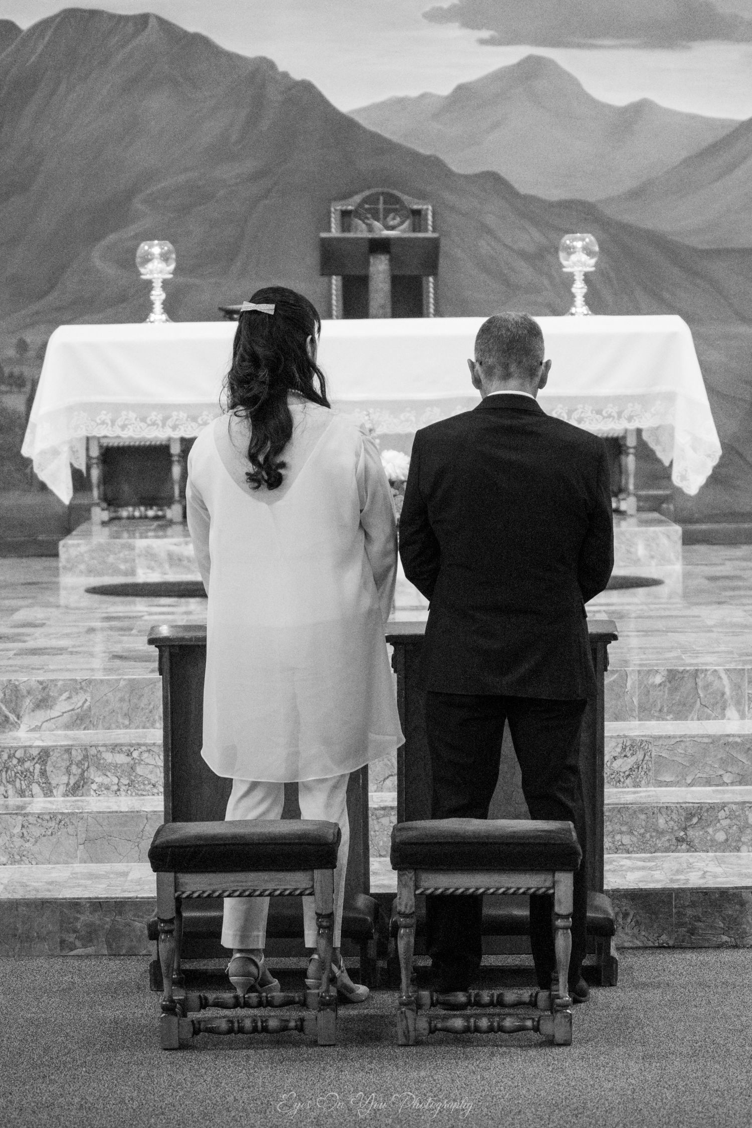 A couple kneels at an outdoor altar with mountain scenery, captured in black and white photography.