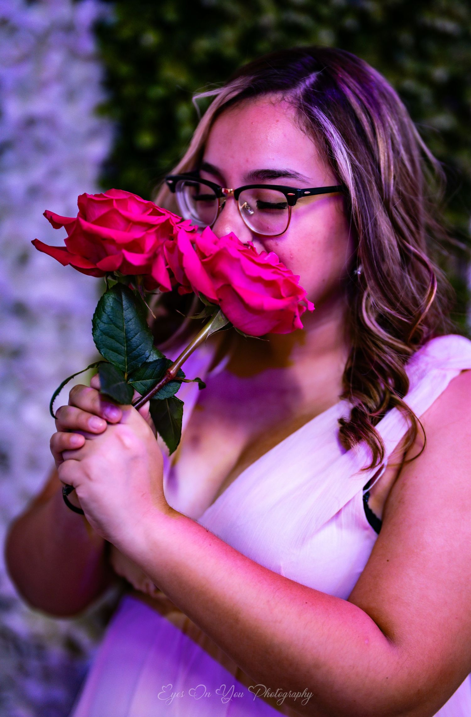 A person in glasses smells a vibrant pink rose in sequence against a purple-tinted background.