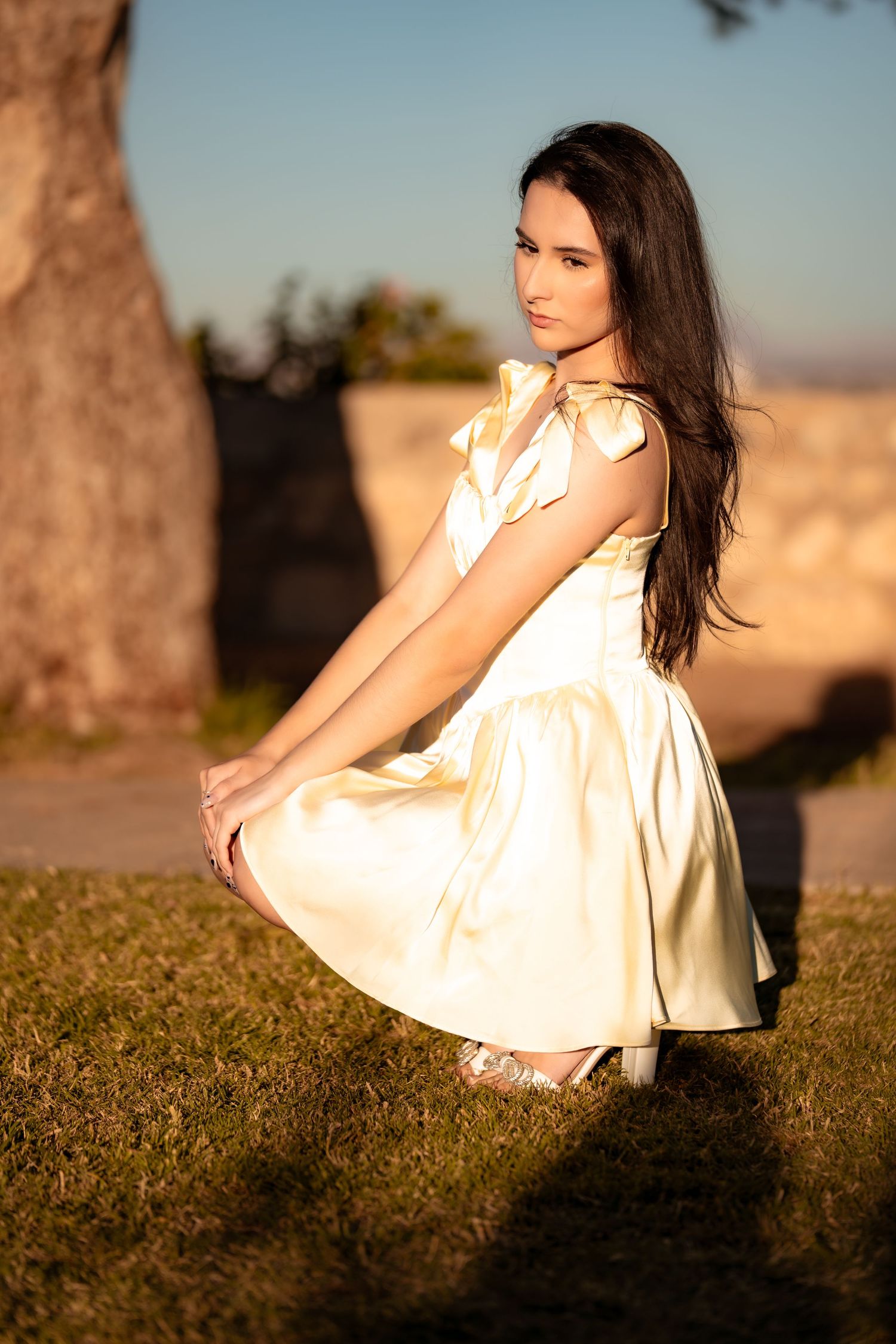 A person in a flowing white dress sits gracefully in a sunlit field of wildflowers during golden hour.