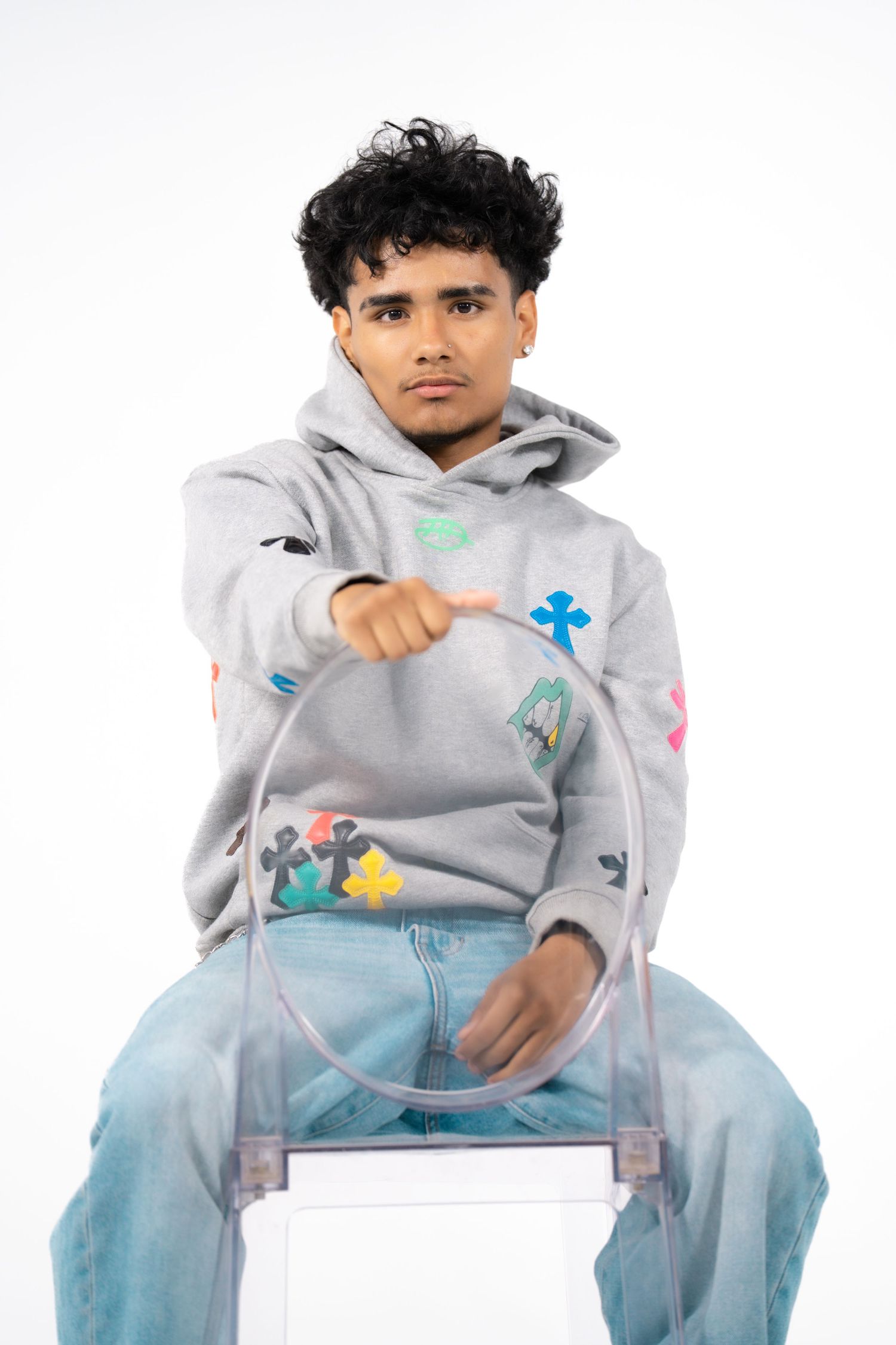 Person wearing a gray hoodie with colorful designs and light blue jeans sits in multiple poses on a white background.
