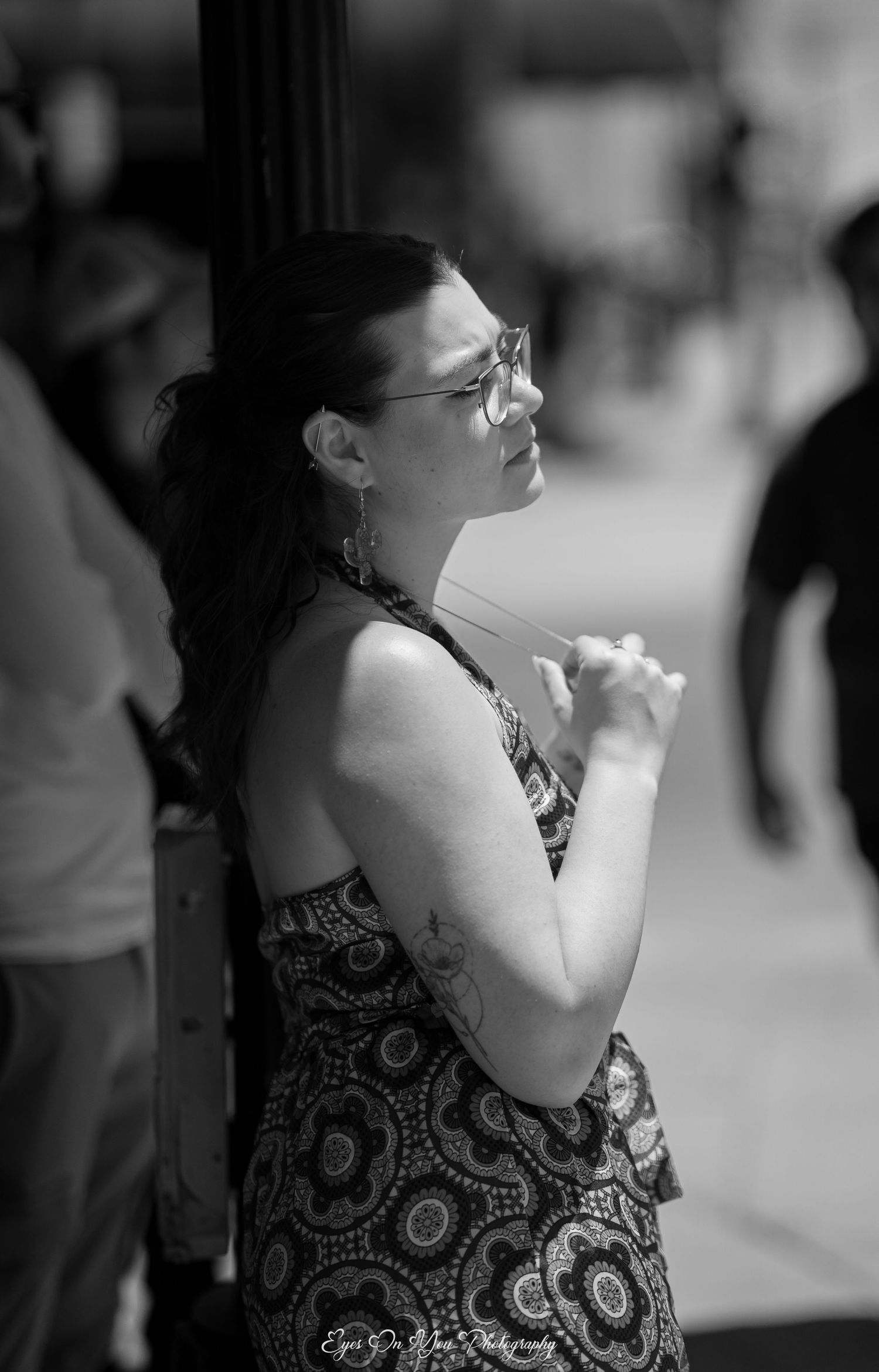 Black and white portrait of someone in a patterned dress leaning against a wall.