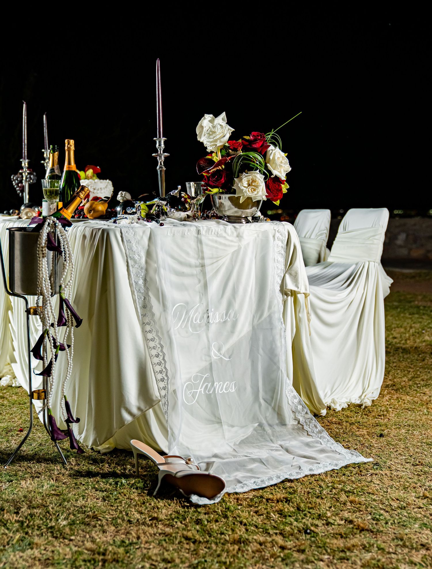 White tablecloths drape over outdoor tables with elegant floral centerpieces and candles for an evening garden reception.