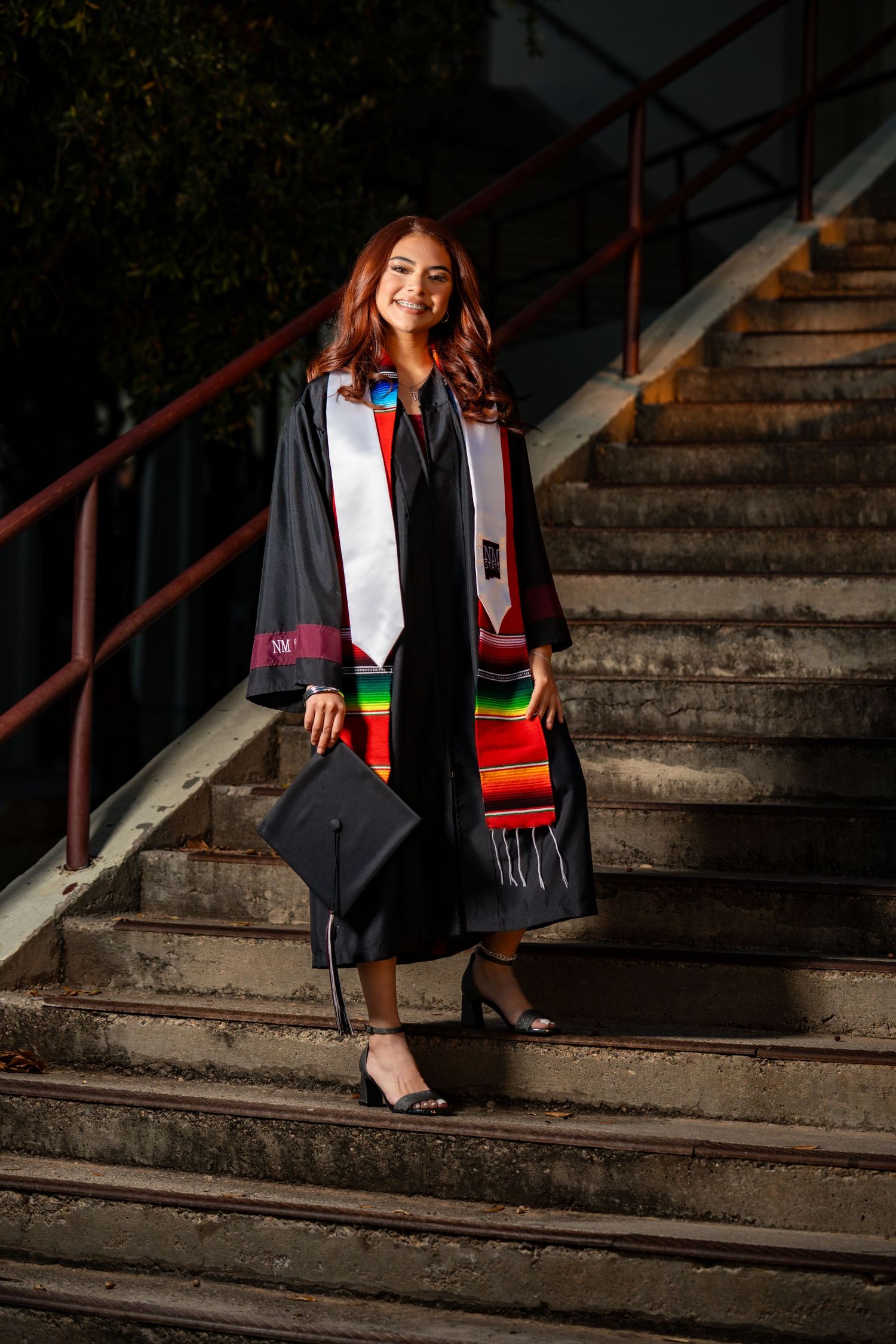 Graduate in academic regalia sits on concrete steps during graduation photoshoot session.