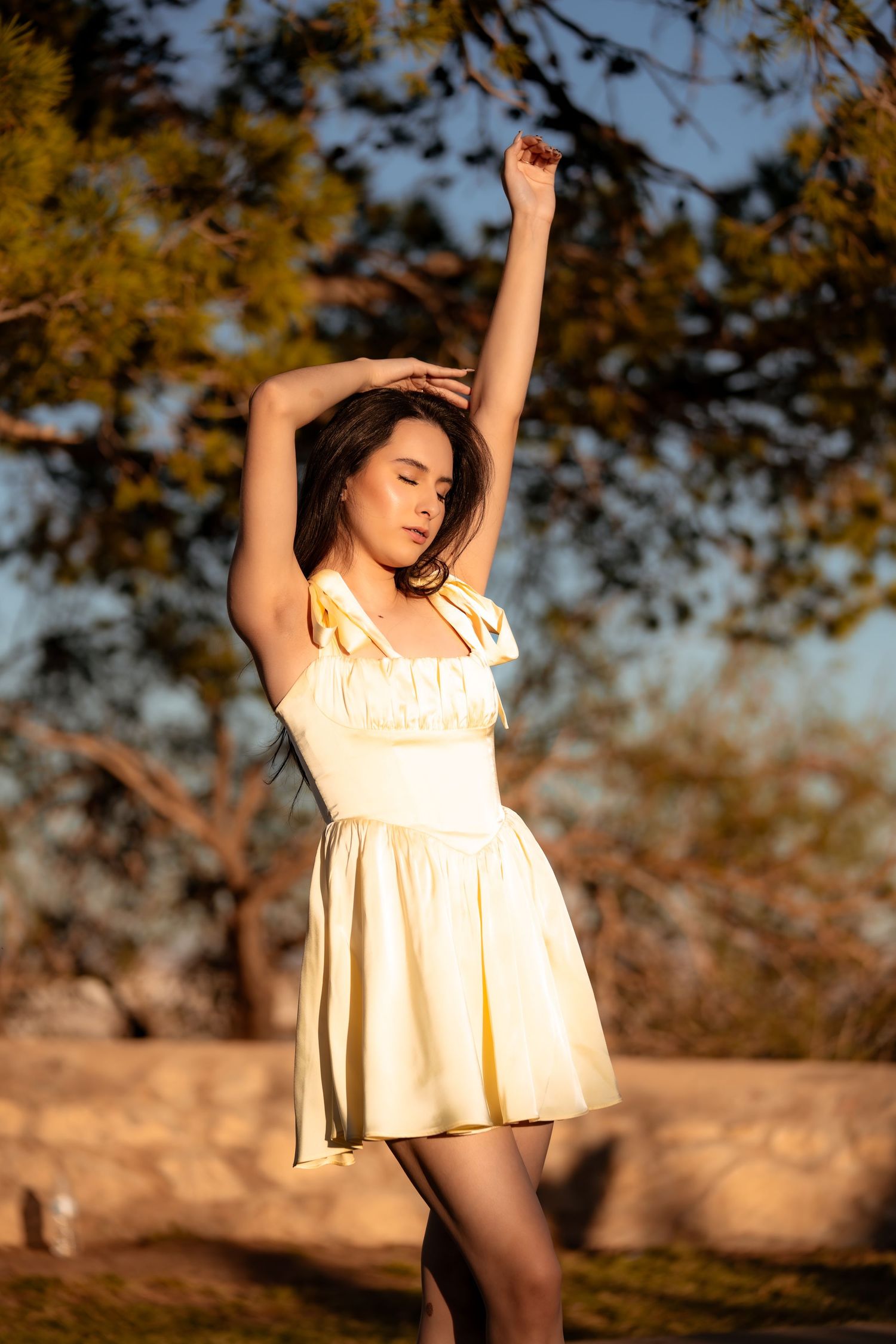 A person in a flowing white dress poses gracefully at sunset in a desert landscape.