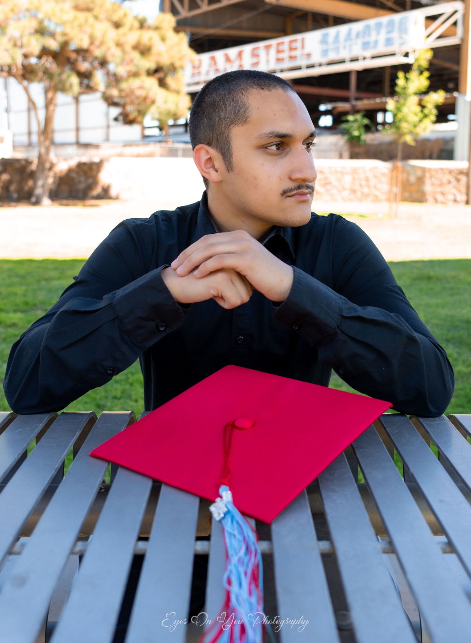 Graduate in dark clothing with red cap resting on wooden bench.