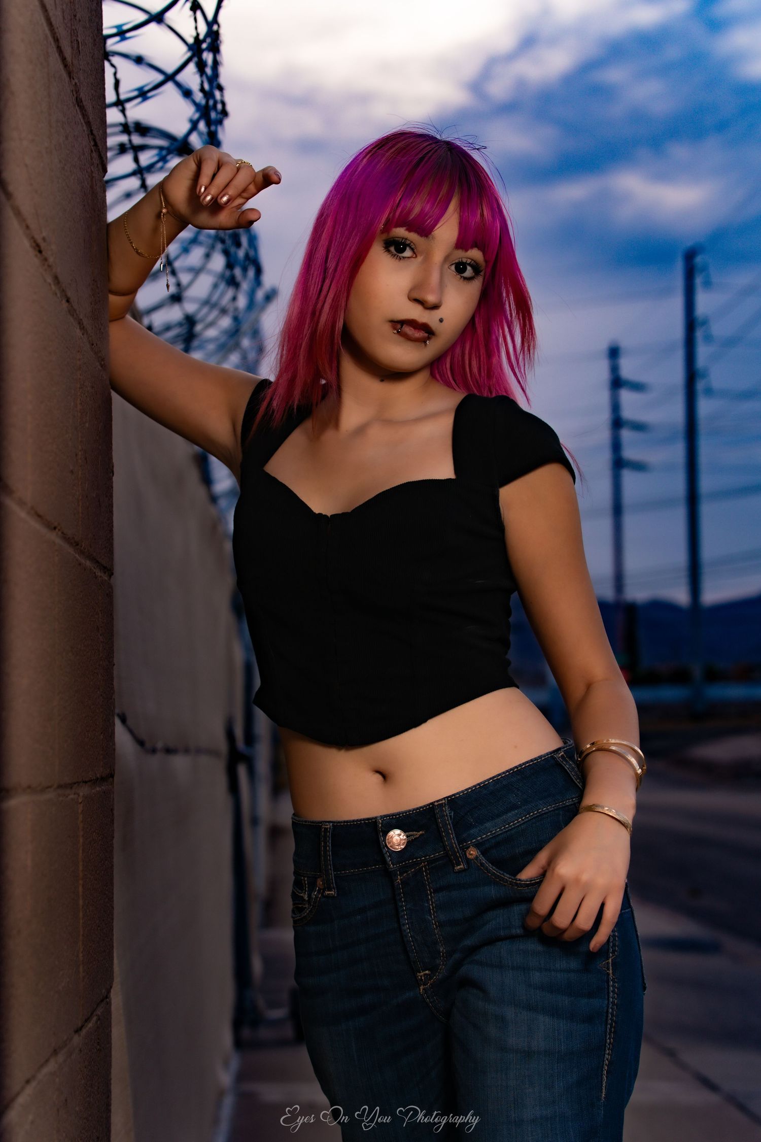 Model with vibrant pink hair poses against industrial backdrop during sunset photoshoot.