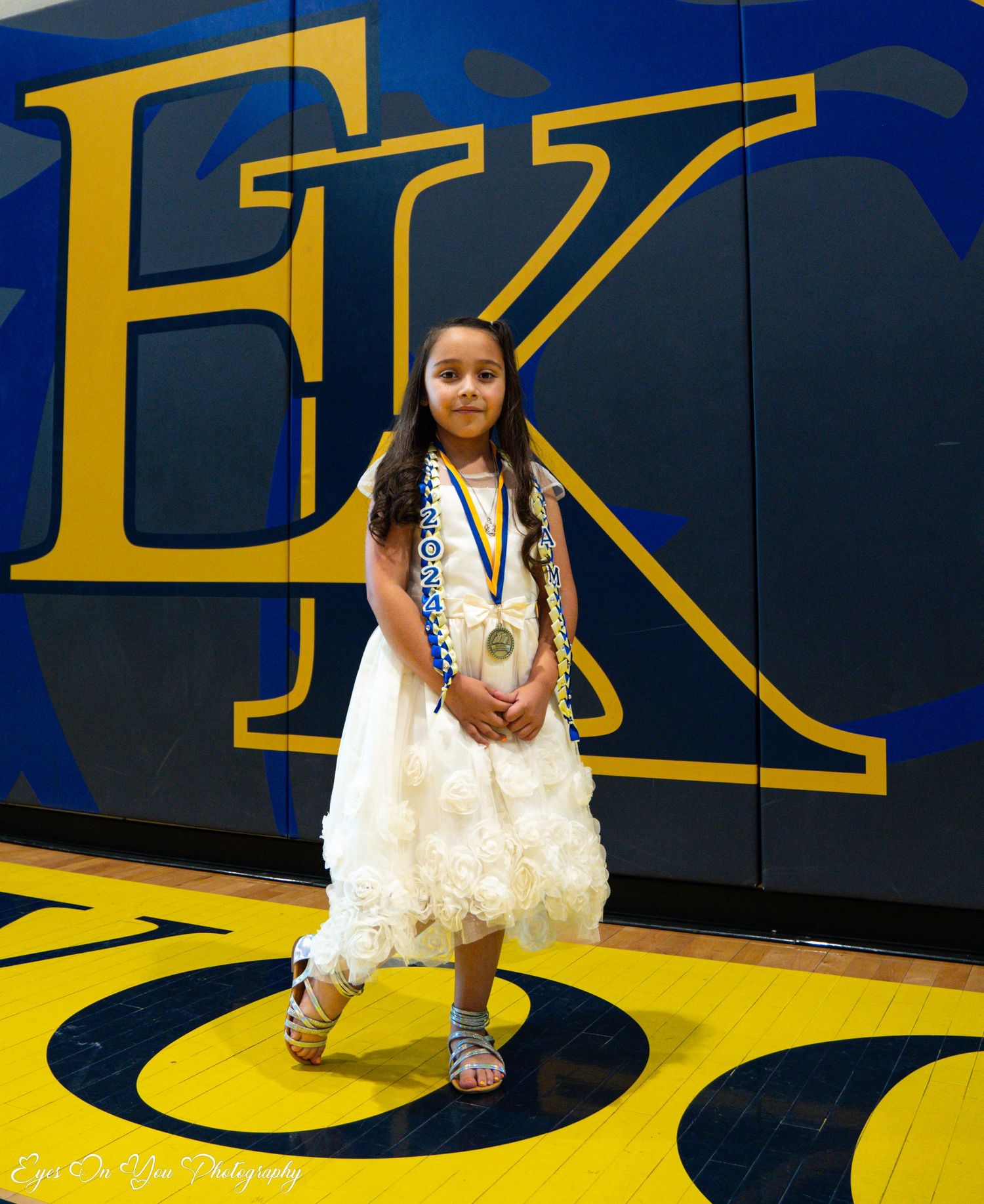 Student poses on yellow and blue gymnasium floor during school celebration.