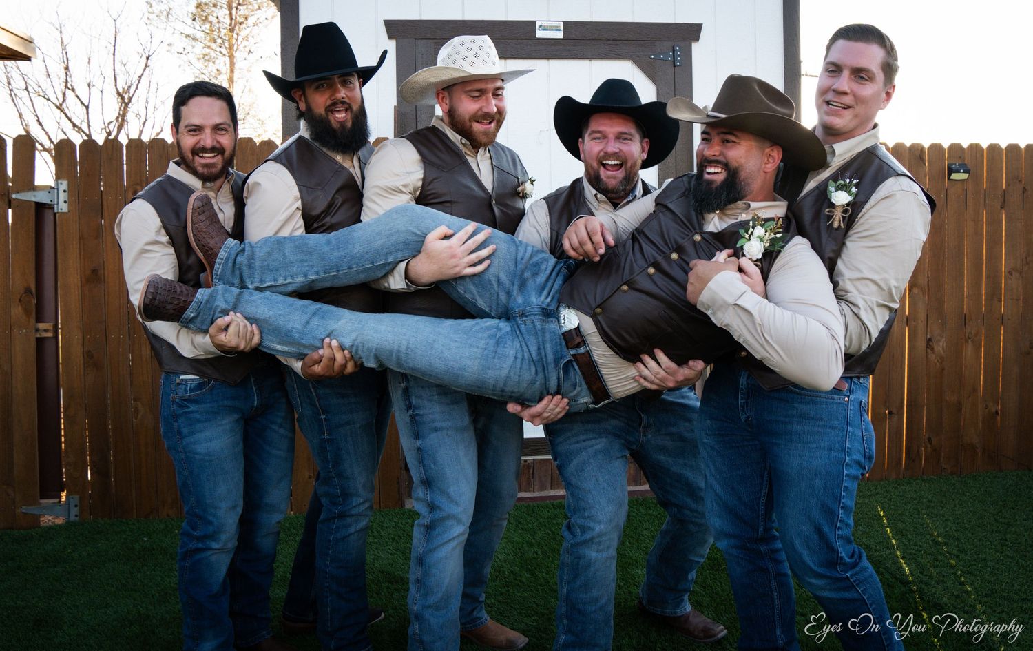 Groomsmen in western attire performing fun poses against a barn backdrop.