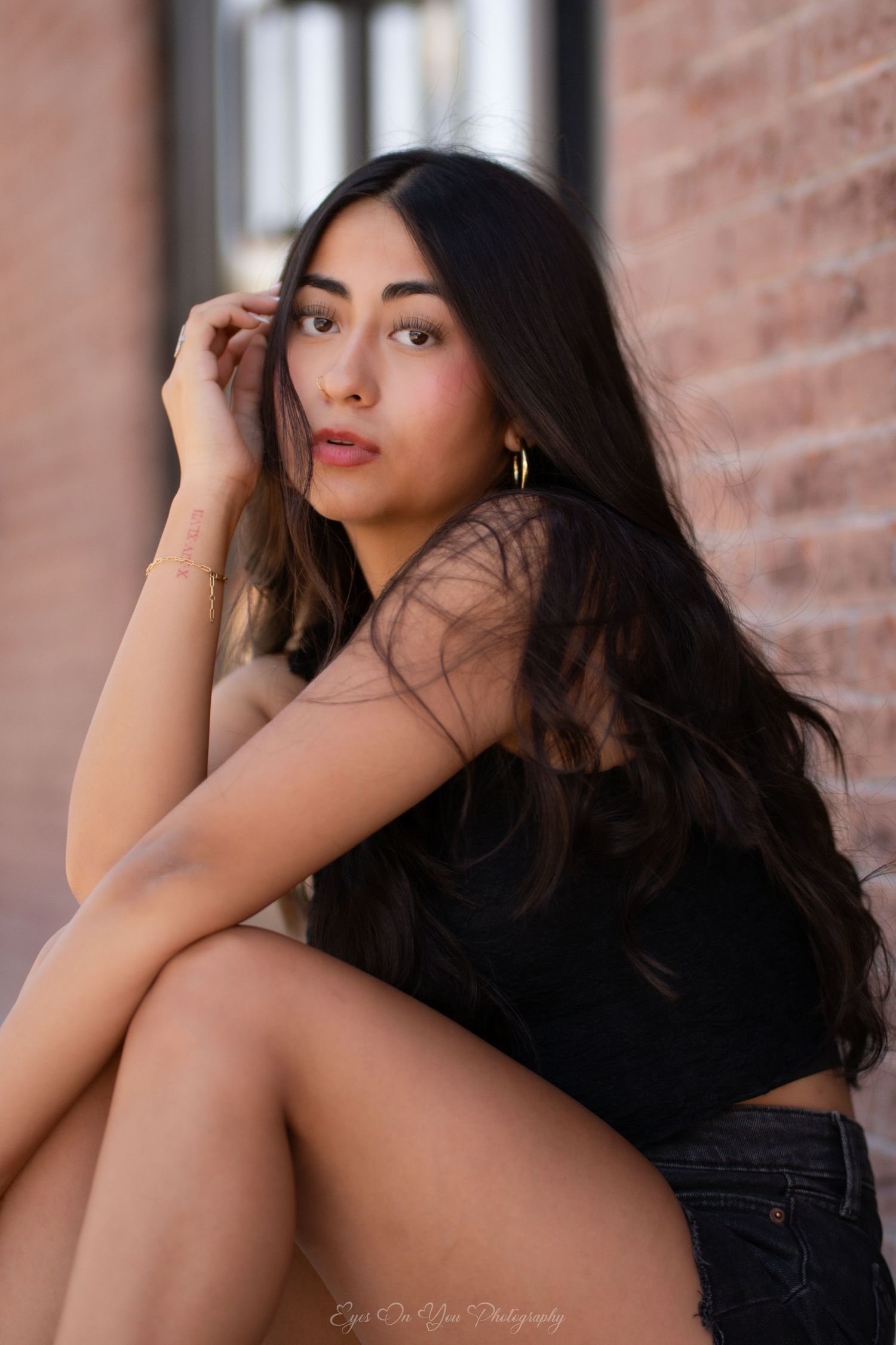 Artistic portrait featuring dark hair and a black outfit against a brick wall backdrop.