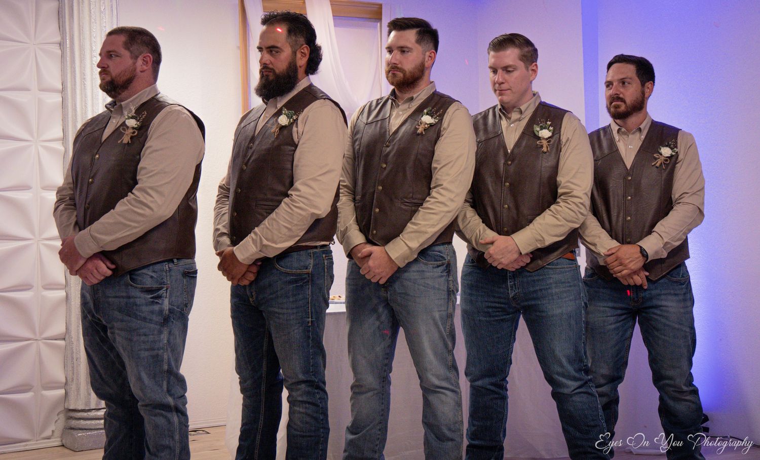 Groomsmen in matching vests and jeans pose in a line for formal wedding photos.