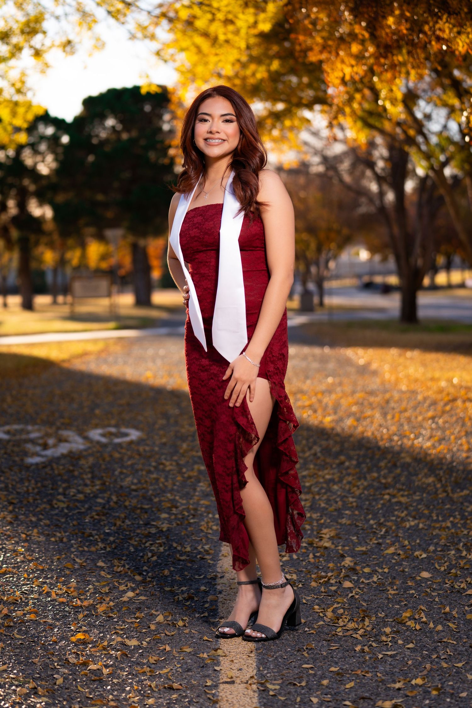 A person in a burgundy dress poses on fallen autumn leaves during golden hour sunset lighting.