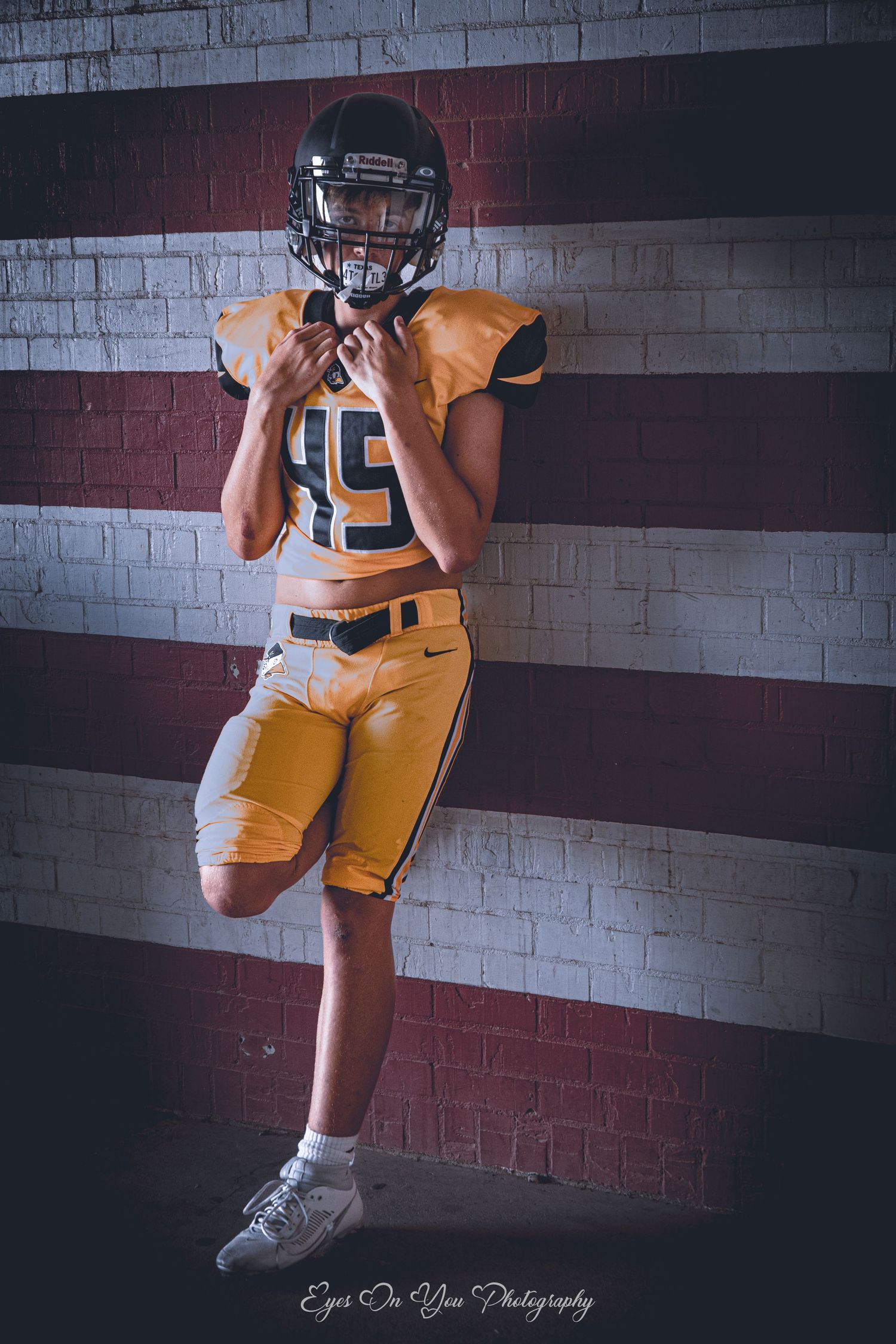 Football player in orange uniform poses against striped wall for athletic portrait.