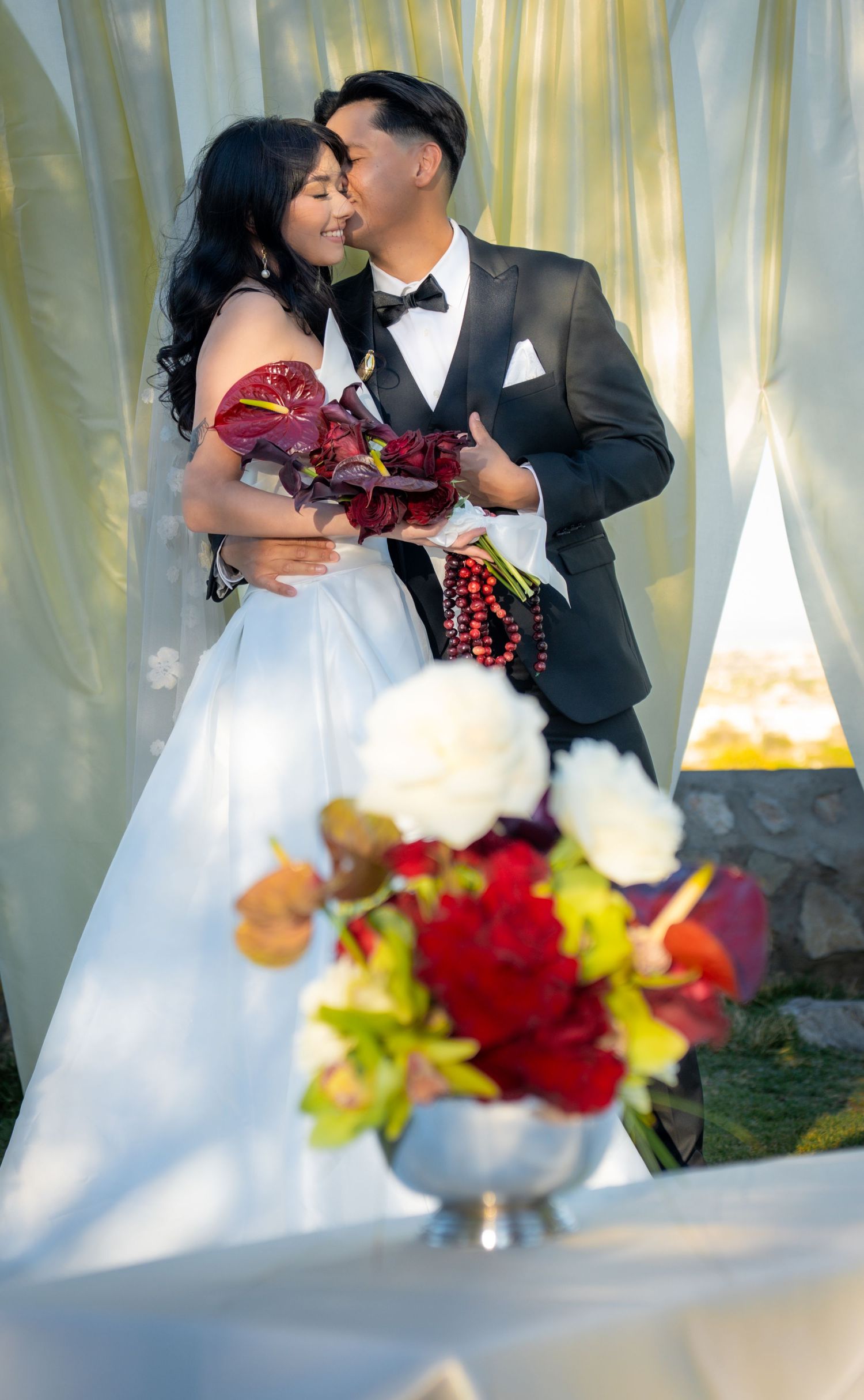 A romantic wedding moment captured with a beautiful floral arrangement of red and white blooms in the foreground.