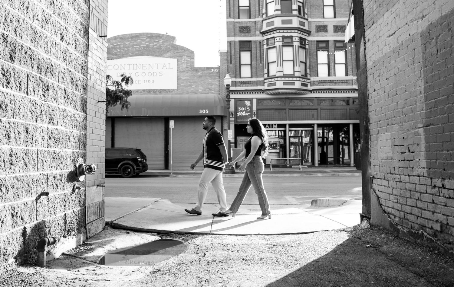 Black and white urban street scene with people walking between brick buildings.