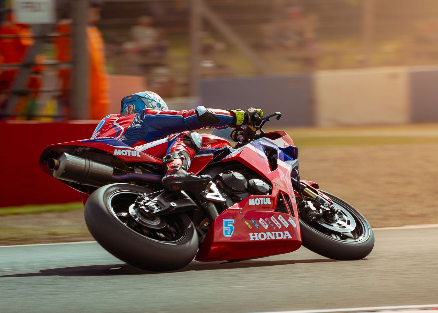 Racing motorcycles compete at sunset on a professional circuit with vibrant orange lighting.