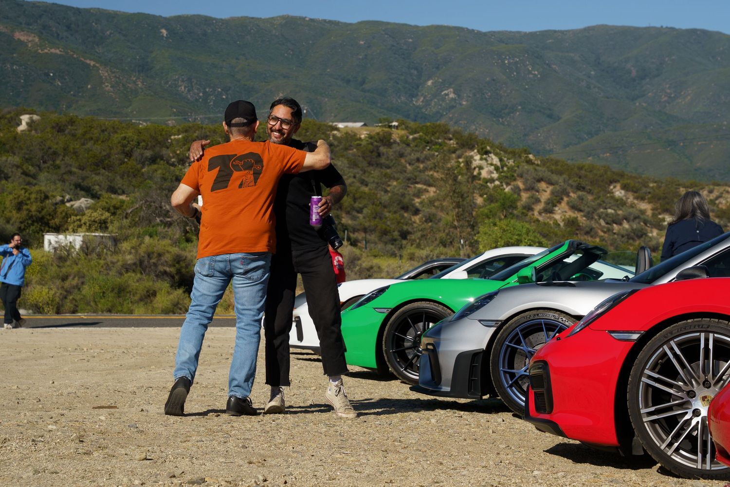 Friends hugging in front of Porsches.