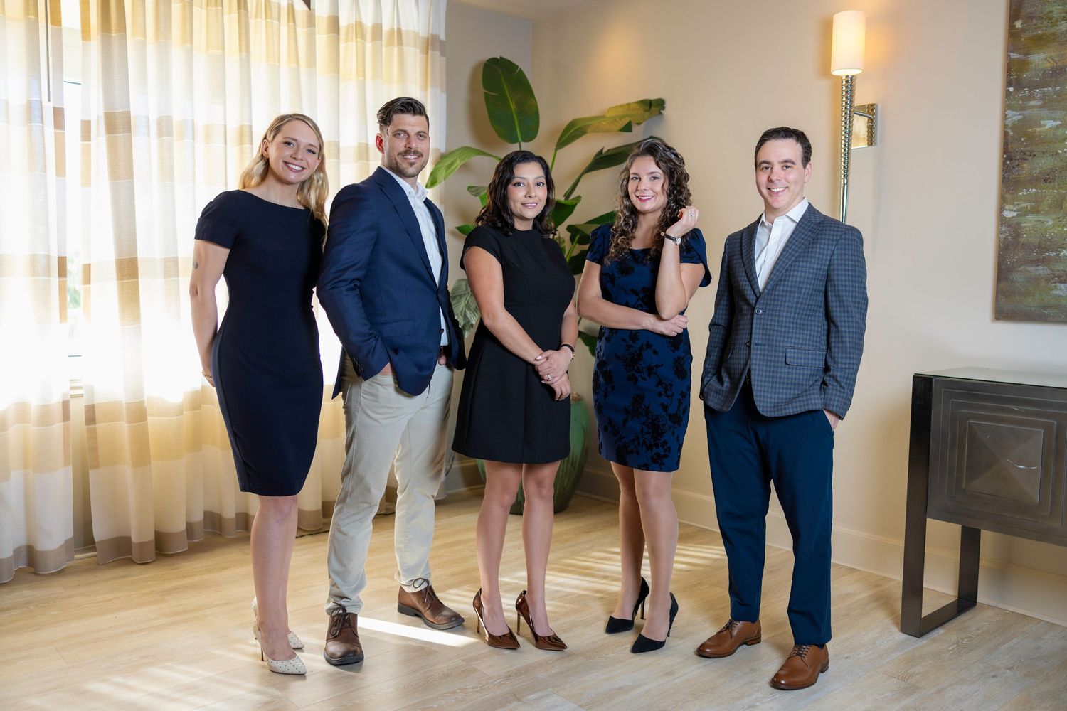 Five professionally dressed real estate team members smiling together in a modern office lobby.