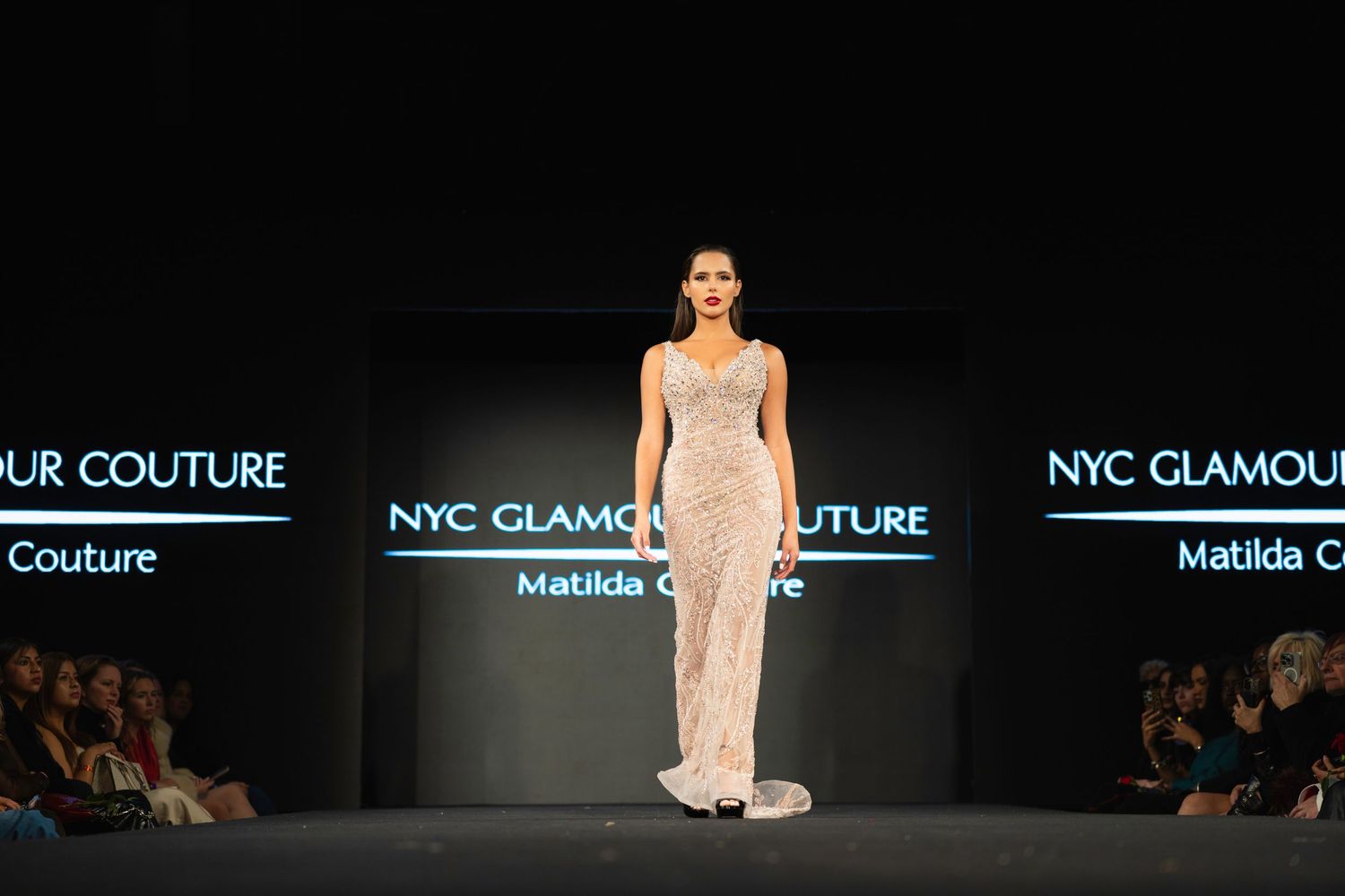 A model wearing a flowing beige evening gown walks the runway during a NYC Glamour fashion show.