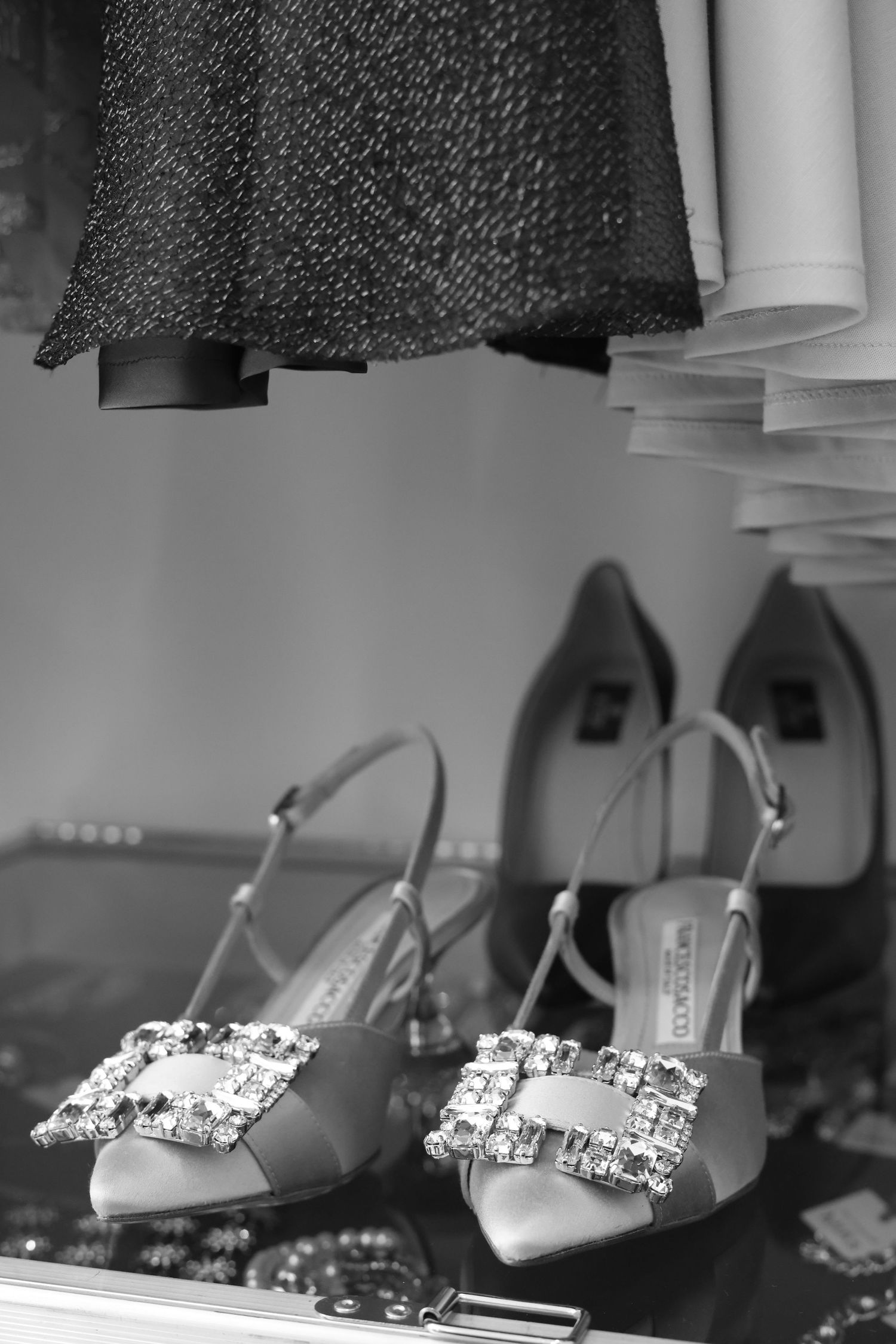 Elegant jewel-encrusted Manolo Blahnik bridal shoes with satin finish and crystal buckle detail shown in black and white.