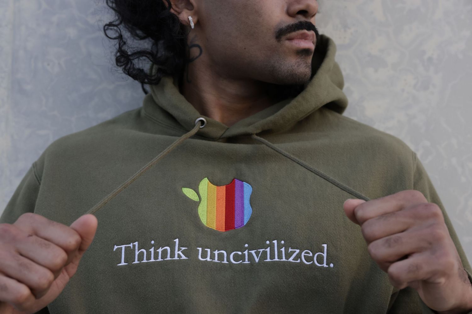 Someone wearing an olive green hoodie with 'Think uncivilized' text and colorful graphic logo on the front.