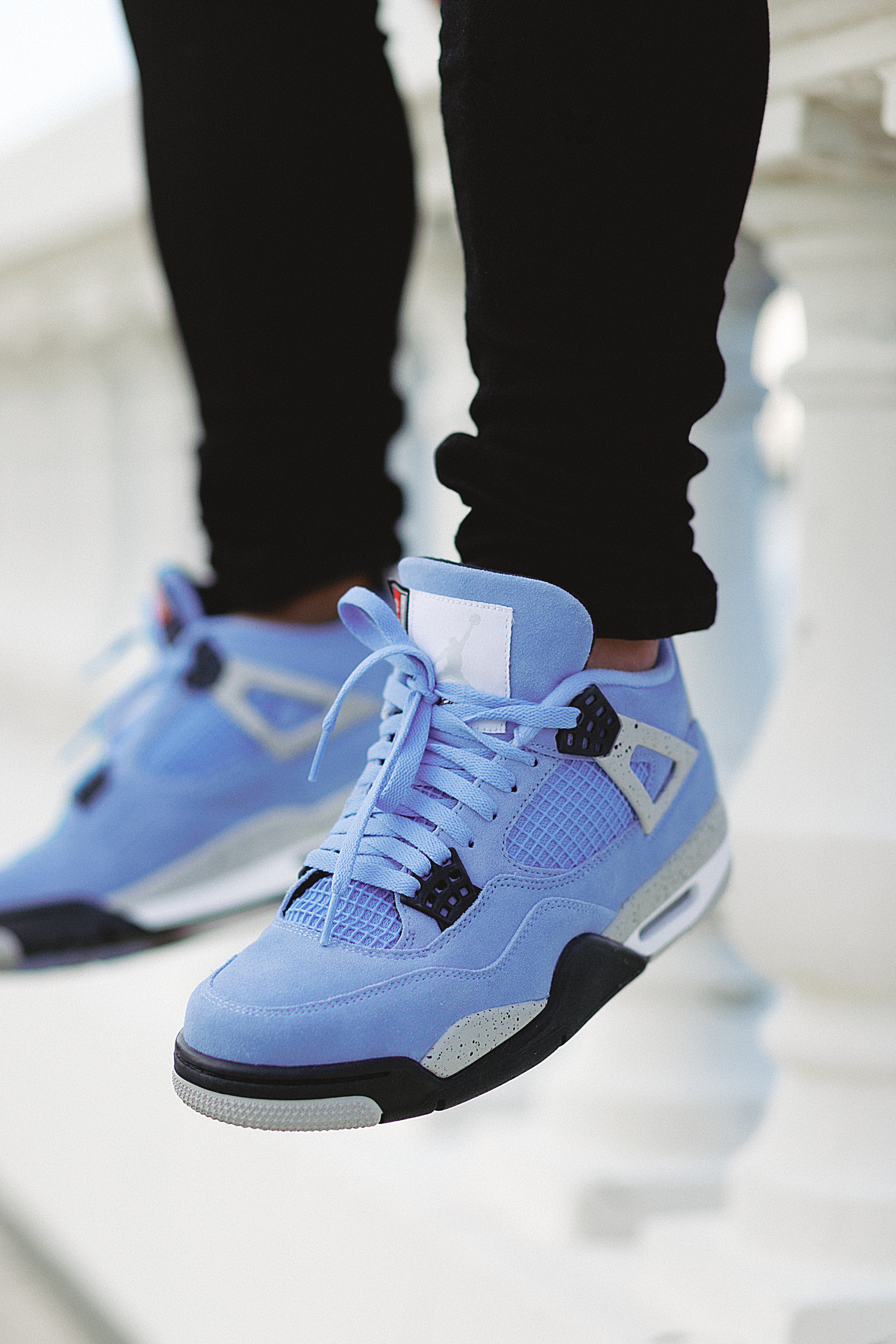 Close-up of light blue Air Jordan 4 sneakers with black and gray accents worn with black pants.